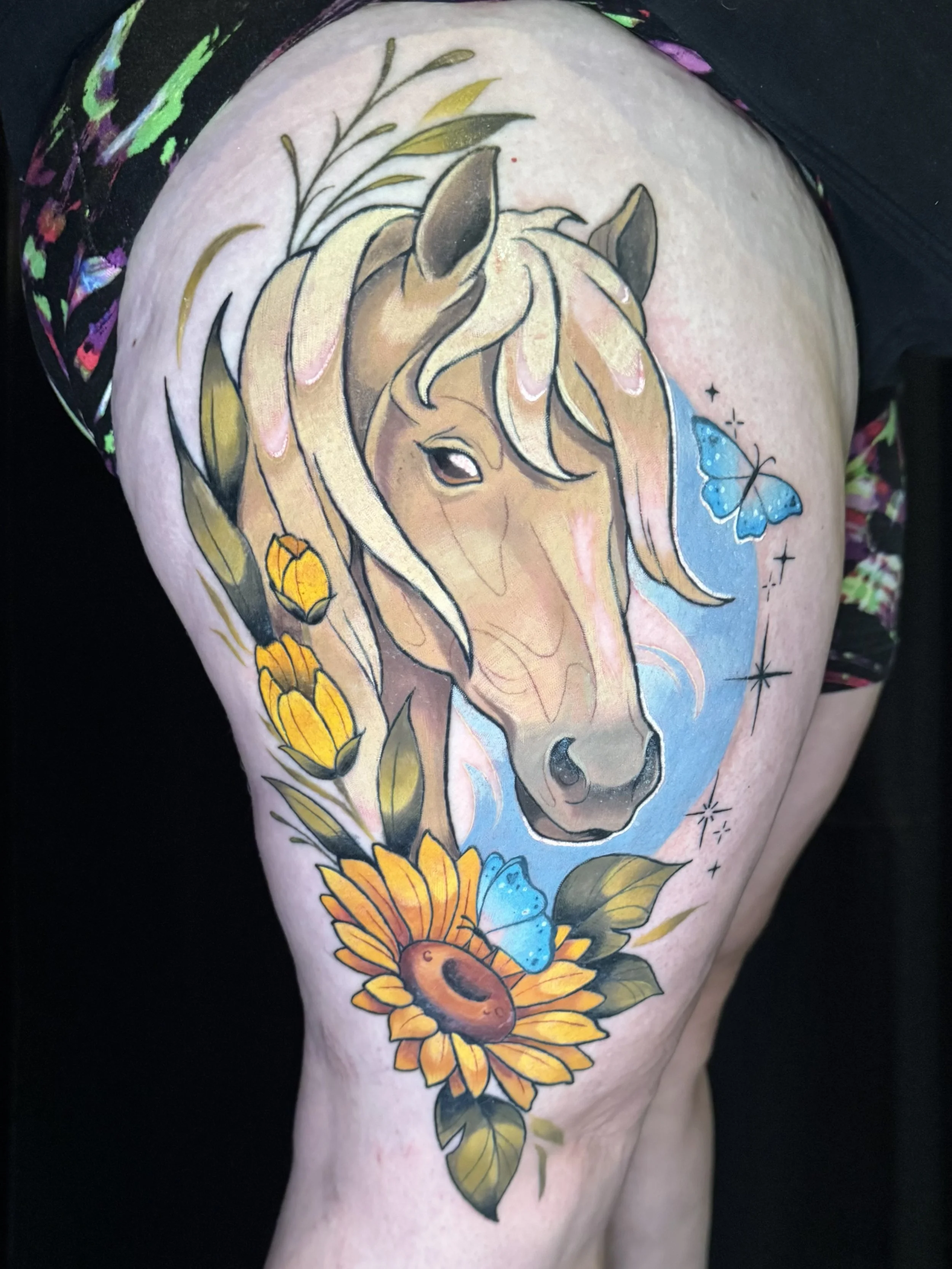 Colorful tattoo of a horse's head with flowers, butterflies, and stars surrounding it.
