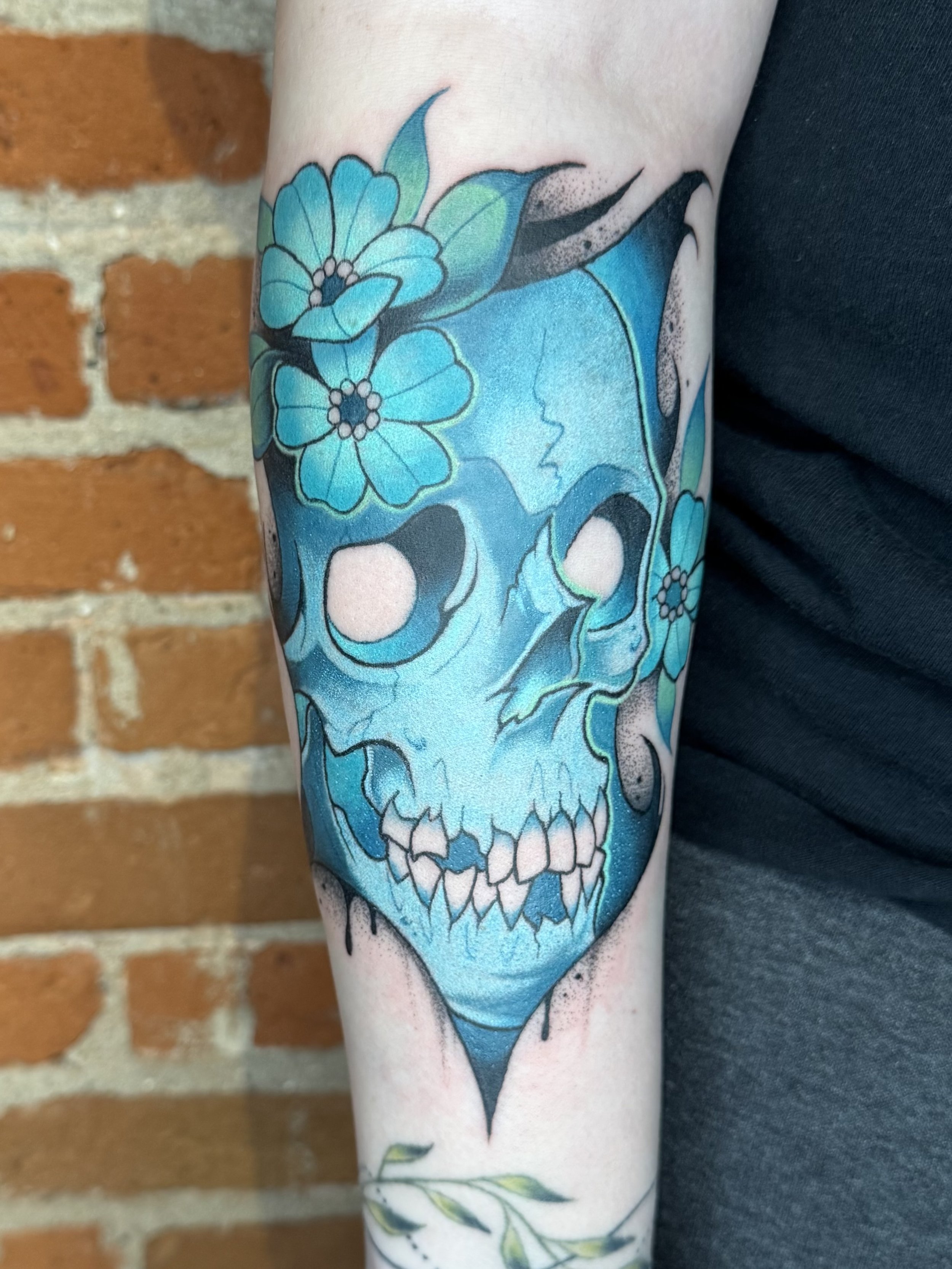 A tattoo of a blue skull with floral and leaf elements on a person's arm.