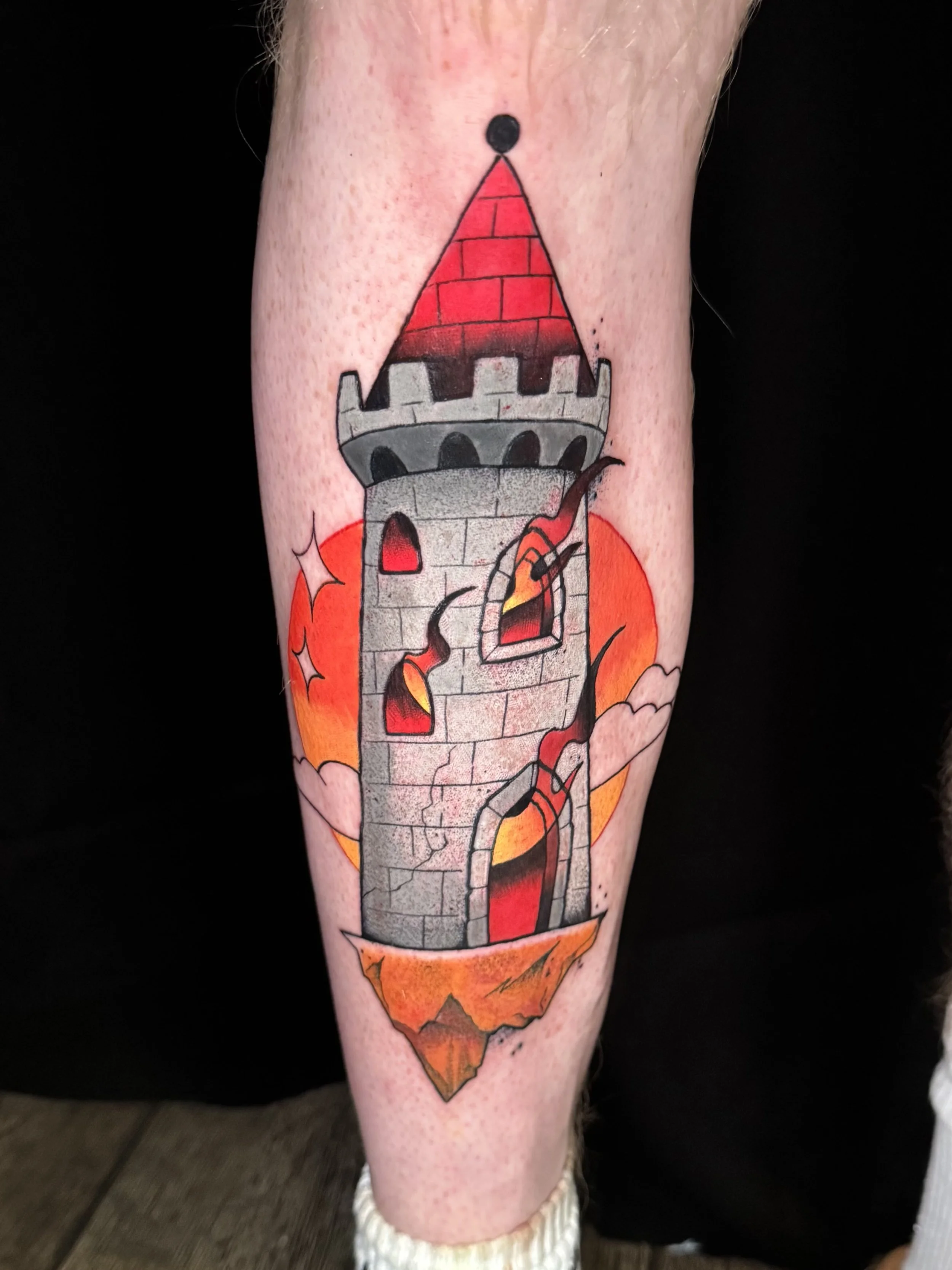 Tattoo of a medieval castle tower with a brick roof, set against a sunset background with clouds and orange hues.