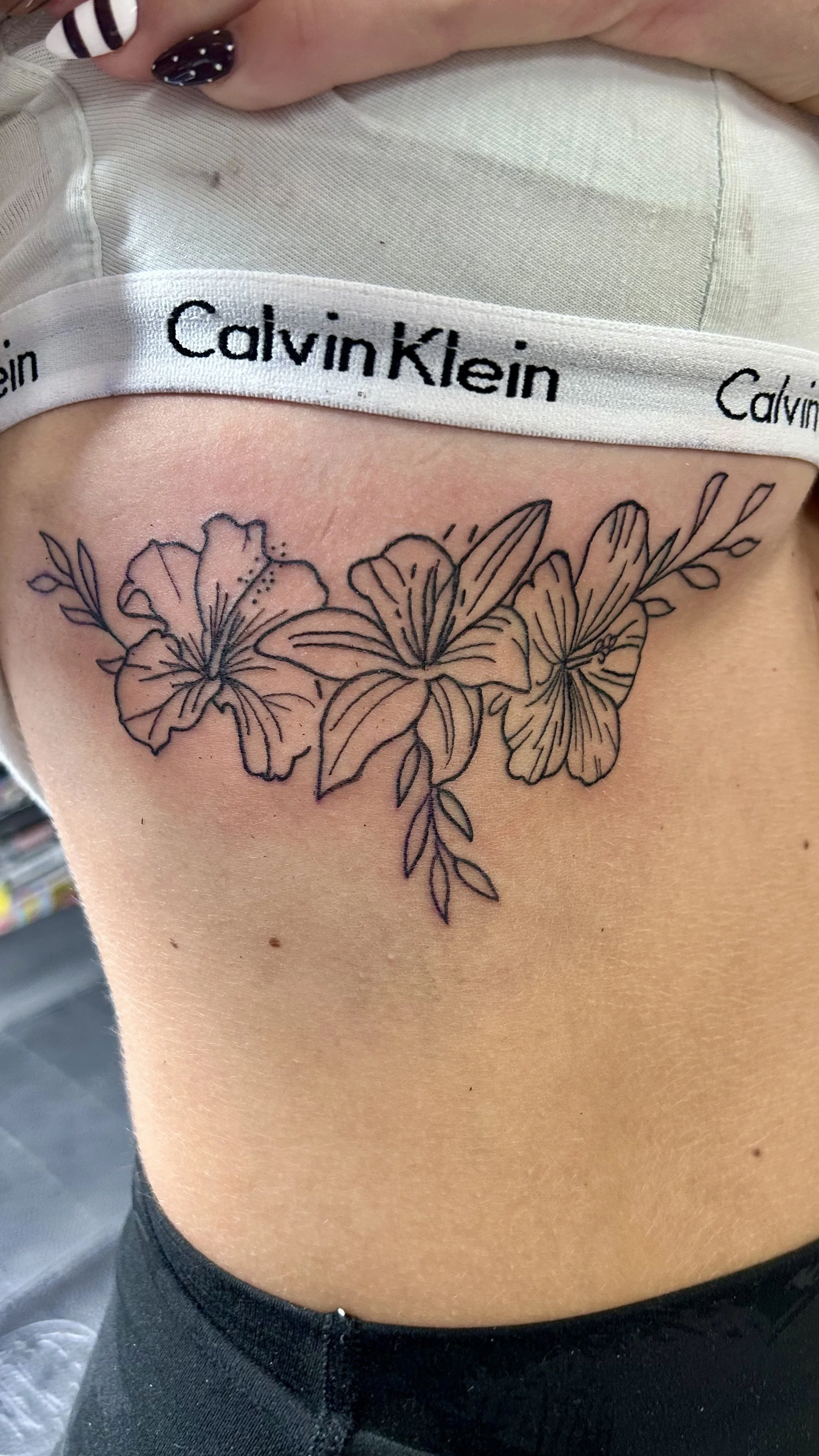 A floral tattoo featuring hibiscus and leaf outlines on a person's side, with Calvin Klein underwear waistband visible.