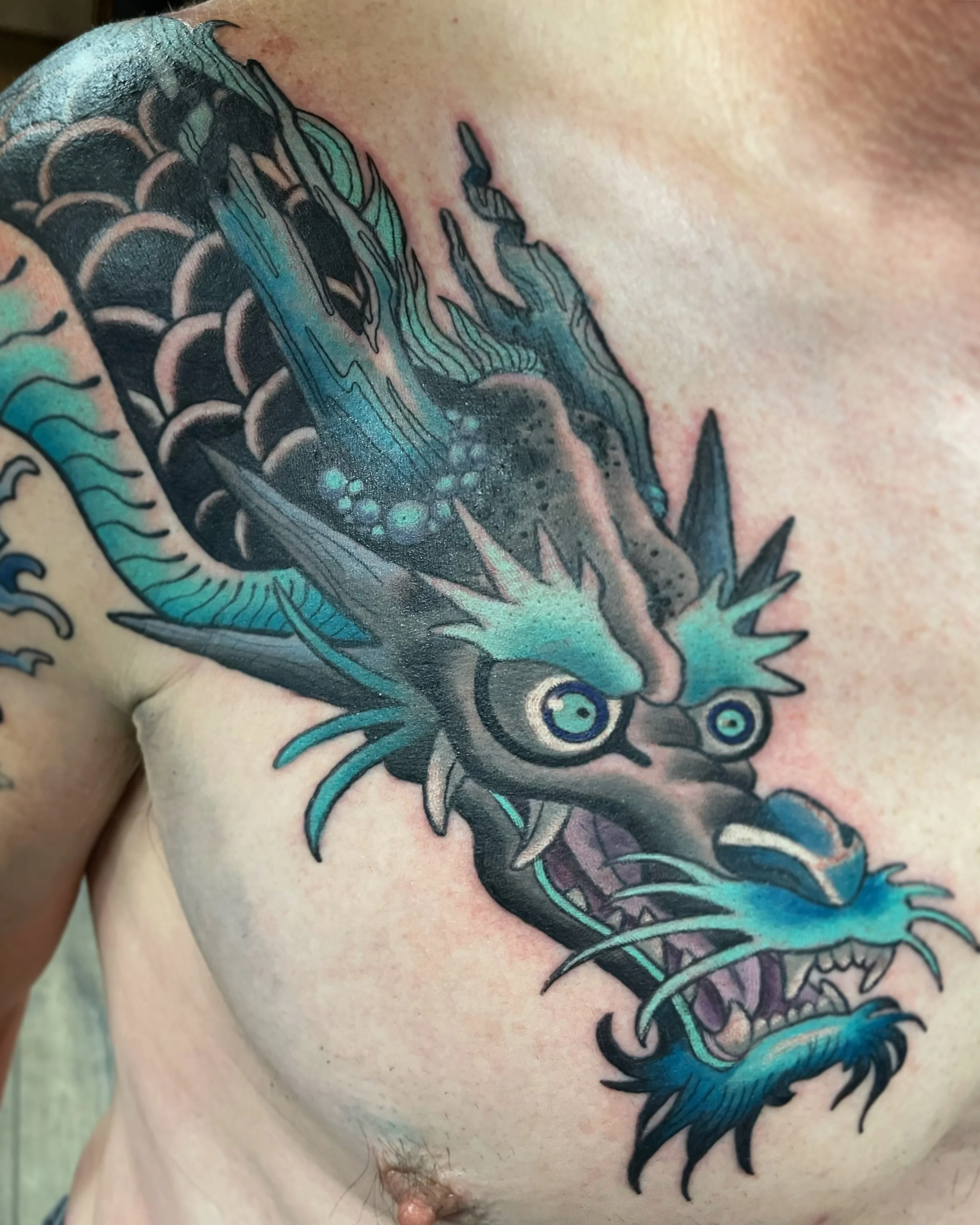 Close-up of a colorful dragon tattoo on a person's shoulder and chest, featuring sharp details and vibrant shades of blue, green, and purple.
