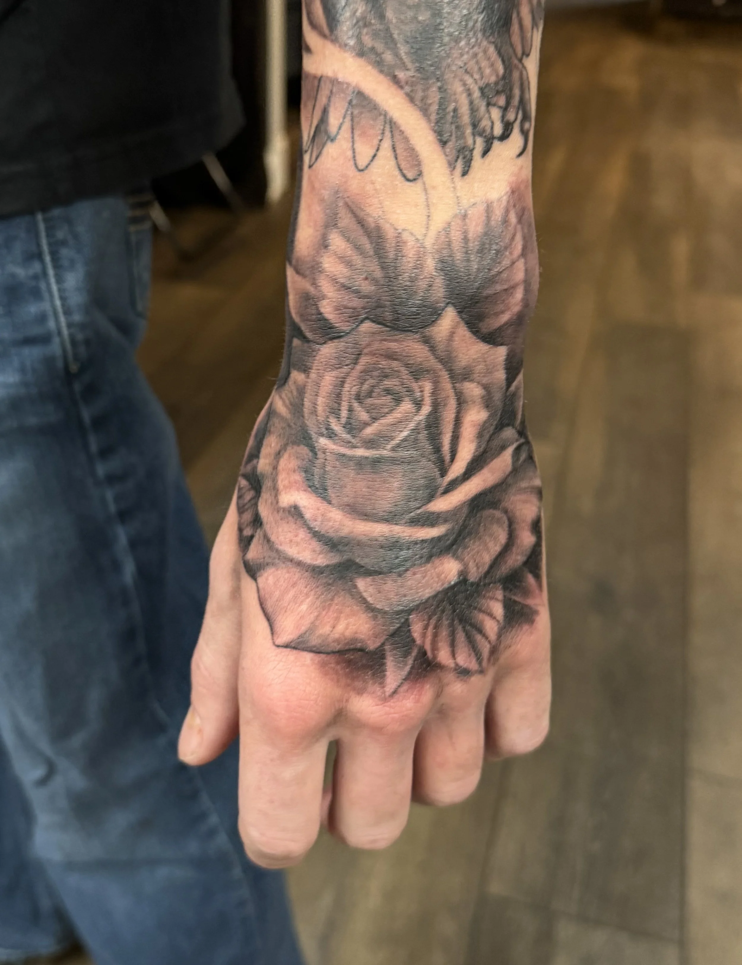 Close-up of a person's hand and arm with a detailed tattoo sleeve featuring flowers and abstract linework.