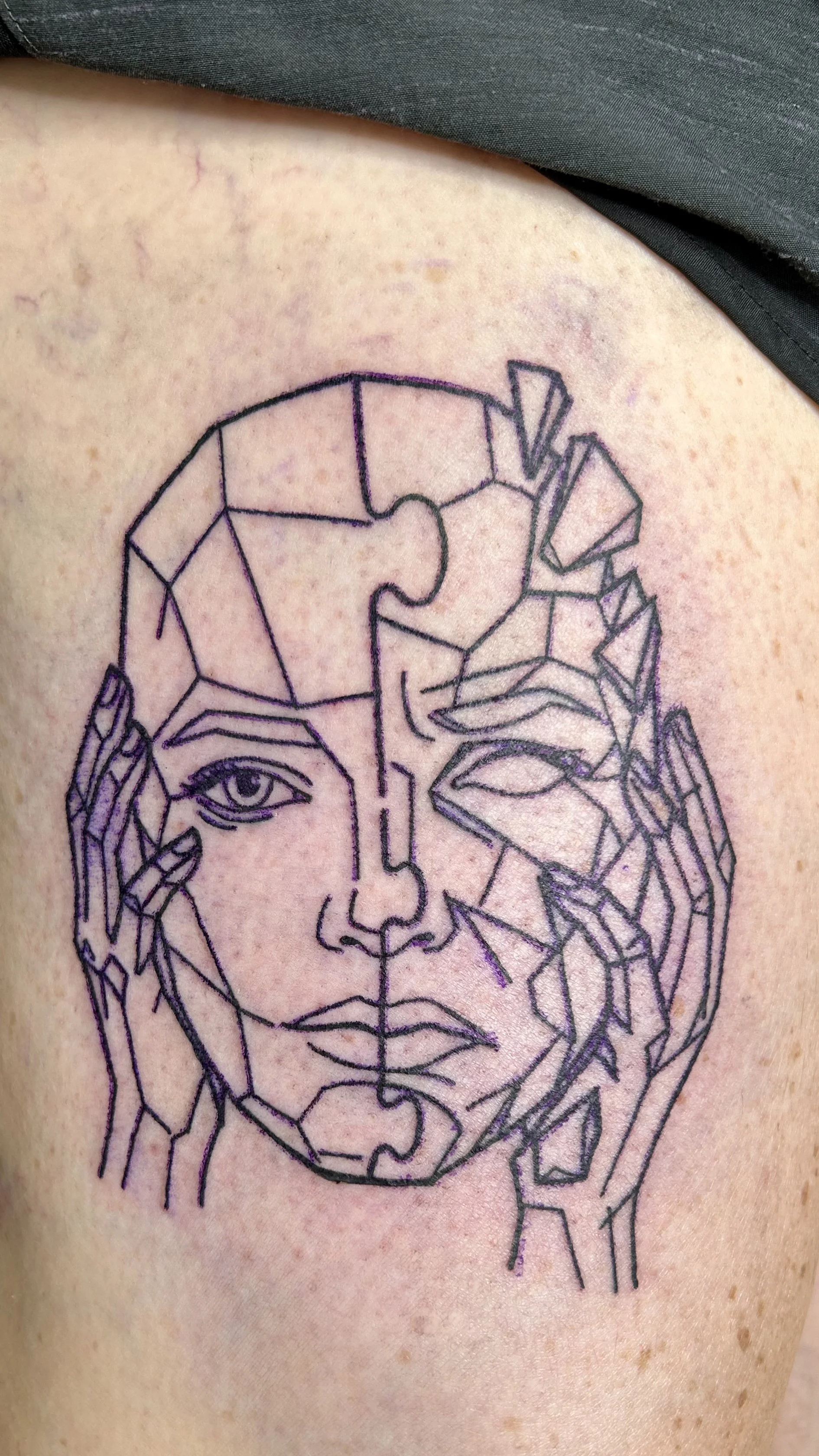 Tattoo of a woman’s face with abstract geometric lines on the arm.