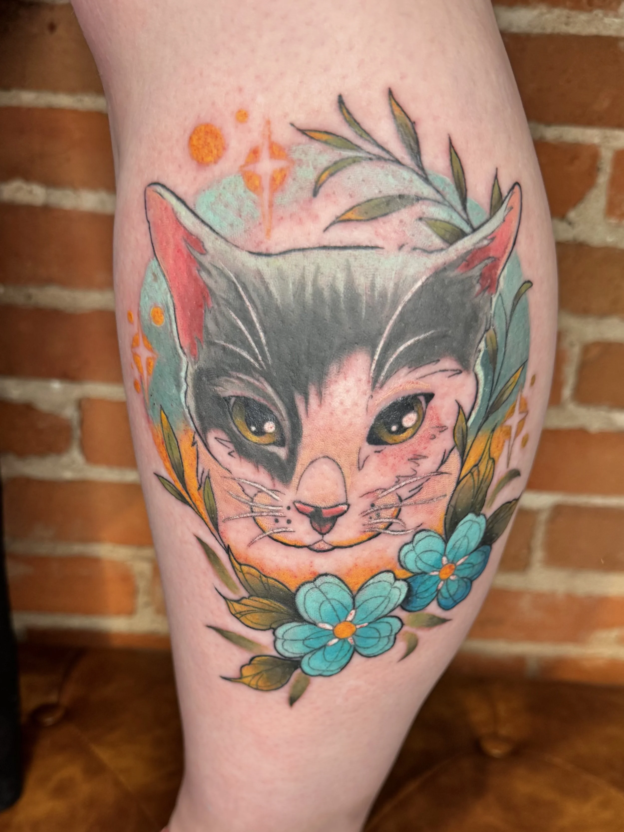 Tattoo of a fox's face, surrounded by blue flowers and green leaves, on a person's arm with a brick wall in the background.