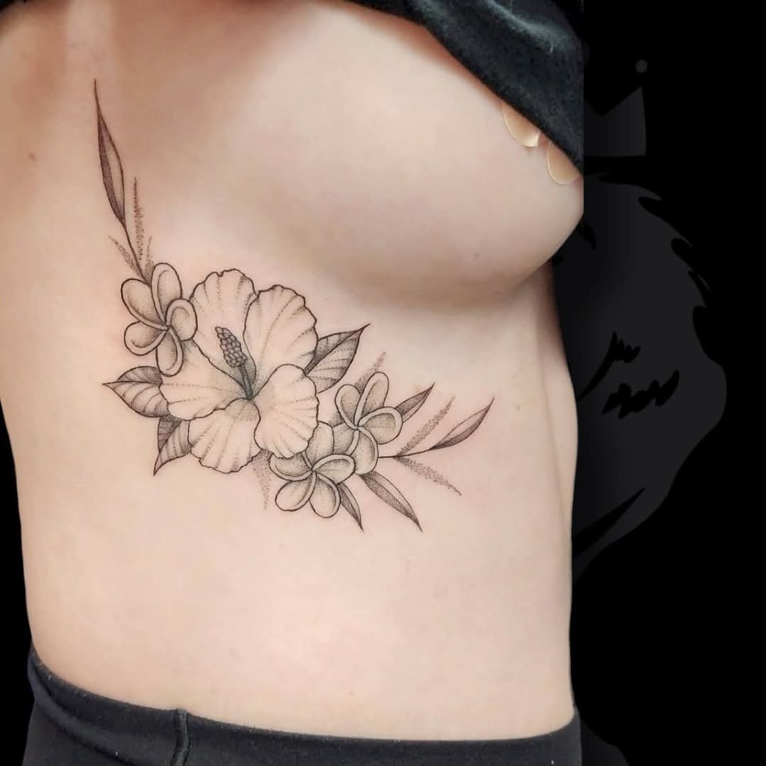 Black and gray floral tattoo on side of person's ribcage featuring hibiscus and plumeria flowers with leaves.