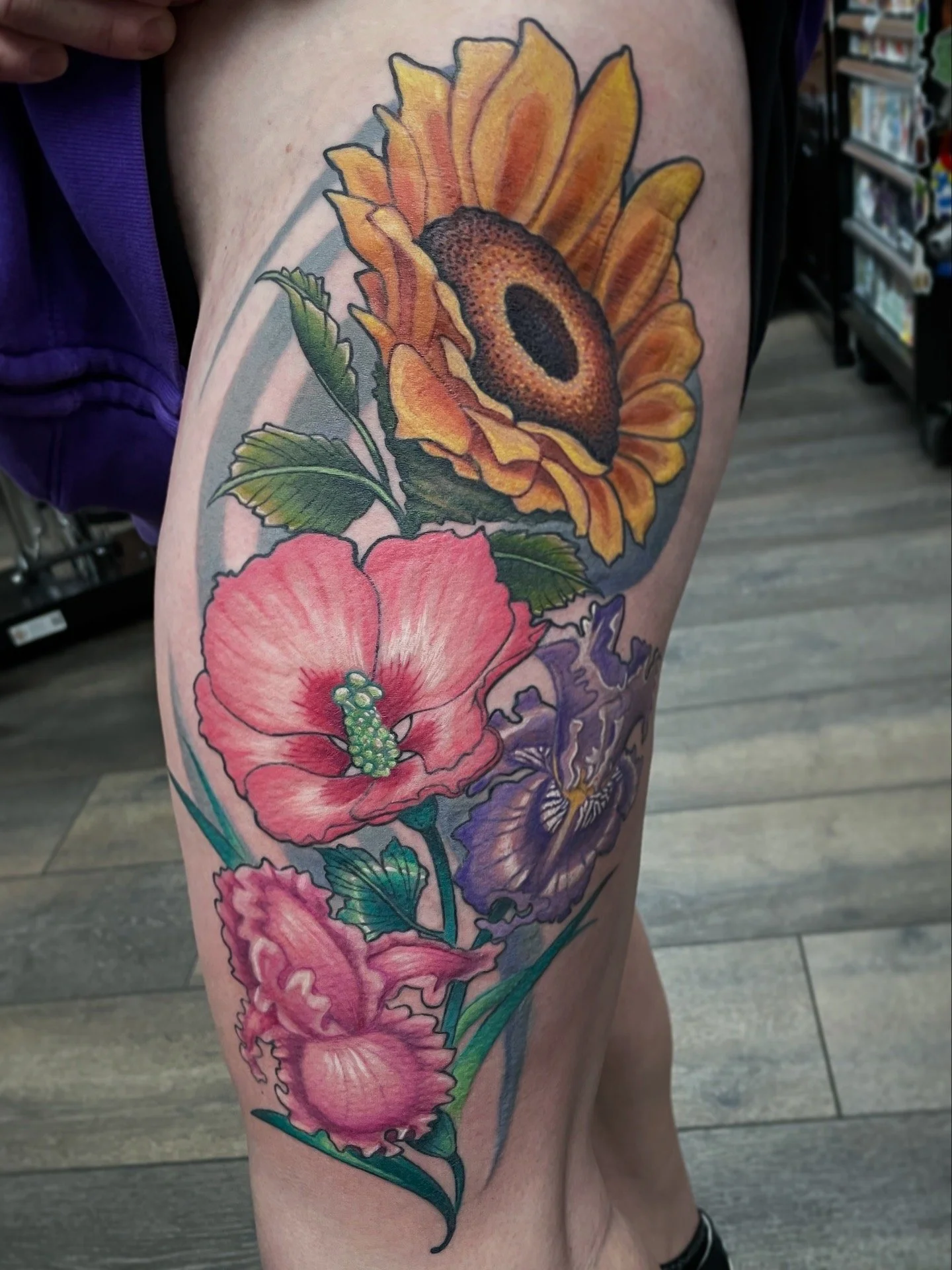 Colorful tattoo of sunflowers and pink hibiscus flowers on a person's thigh.