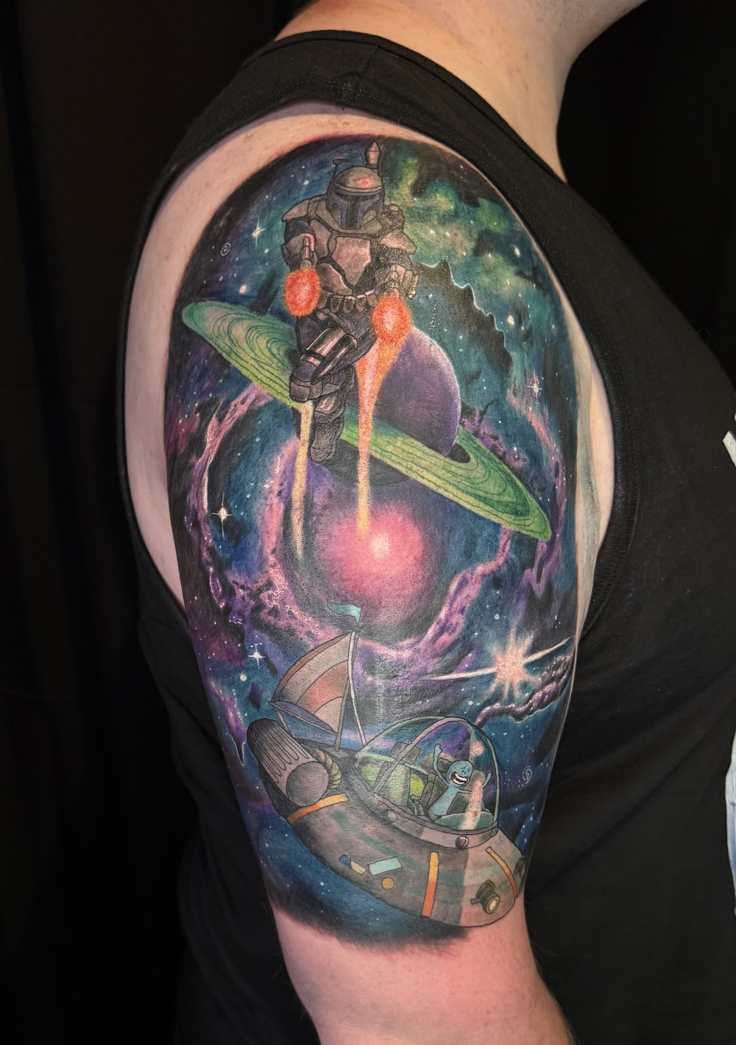 Colorful tattoo on upper arm featuring Boba Fett from Star Wars riding a spaceship through a galaxy scene with planets, stars, and cosmic clouds.