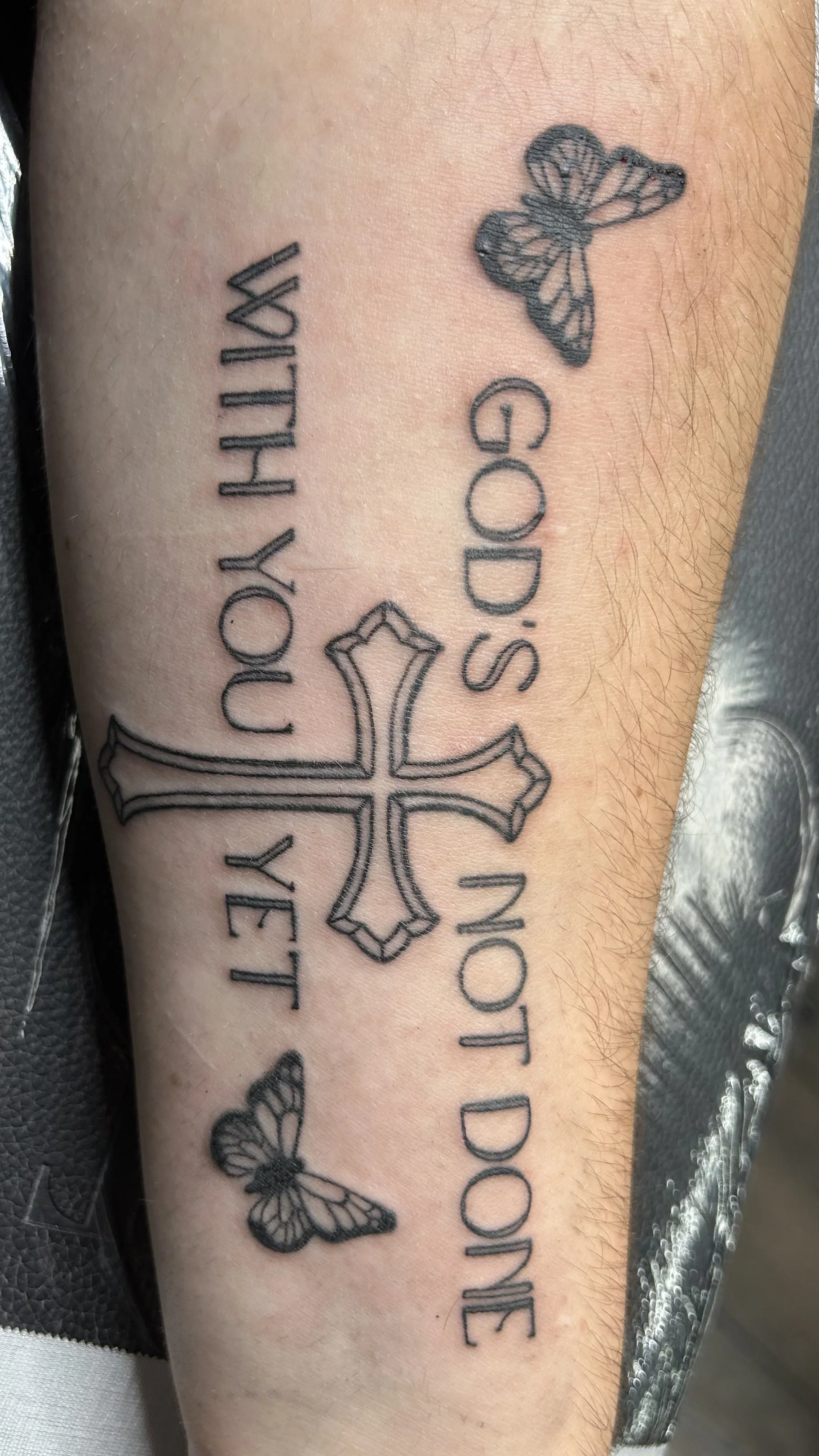 Tattoo of a butterfly, a cross, and text on a person's arm.