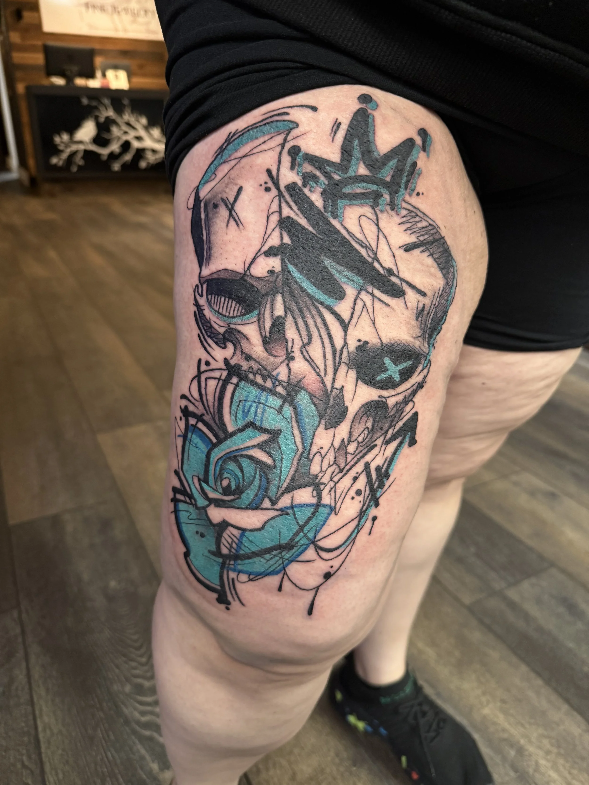 Tattoo of a stylized face with abstract elements and blue accents on a person's upper thigh.