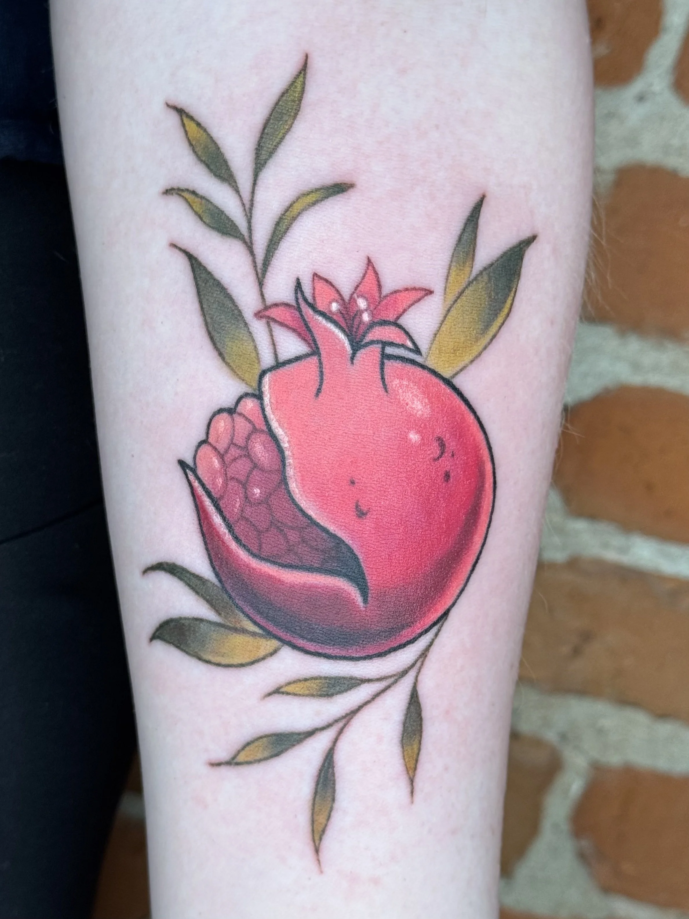 Close-up of a colorful tattoo of a pomegranate with leaves and a pink flower on skin.