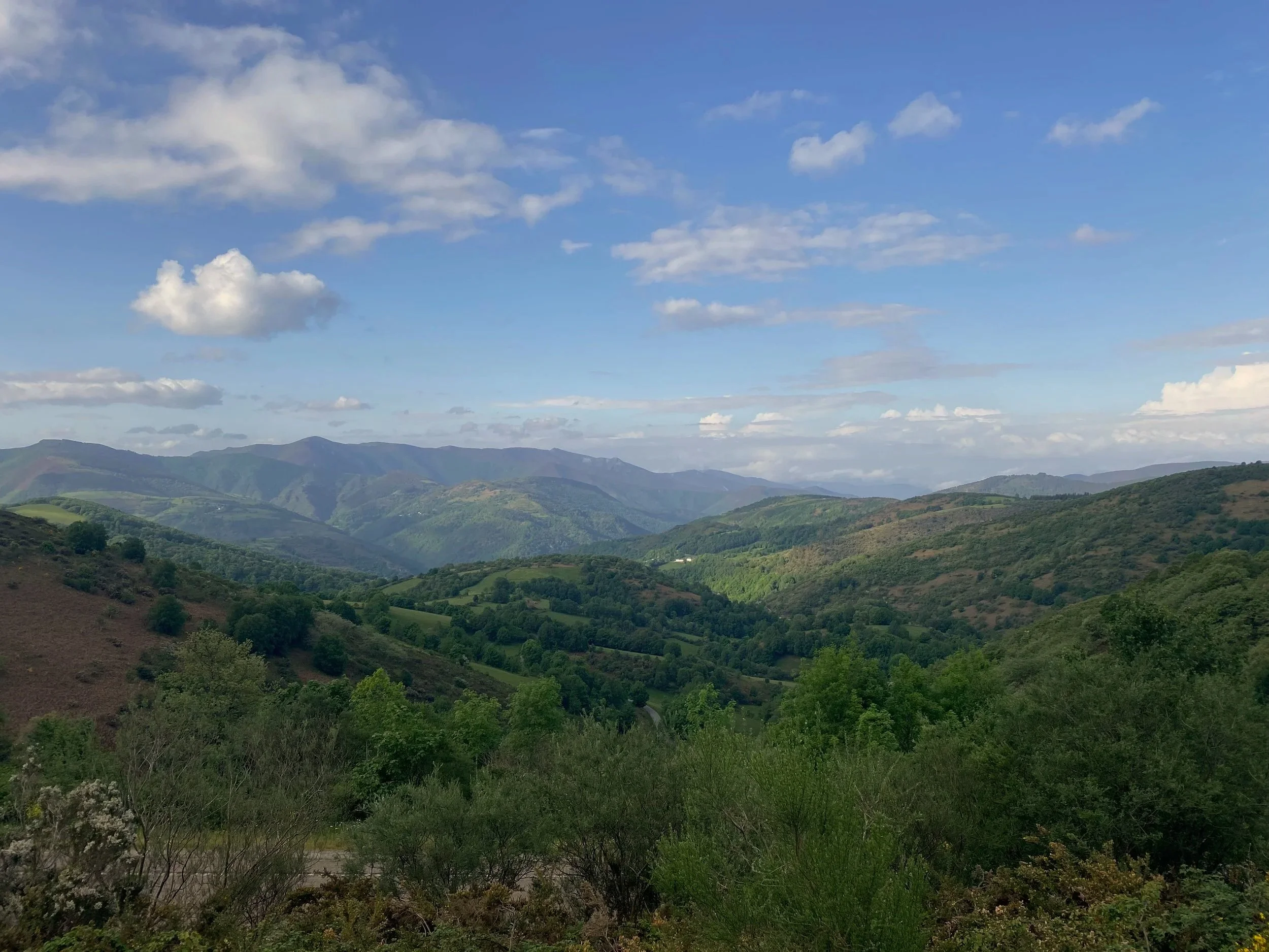 A panoramic view of green rolling hills and mountains under a blue sky with scattered clouds.
