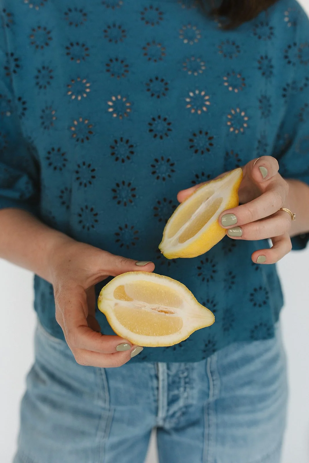 Person holding two lemon halves, one yellow and one light green, with a blue patterned shirt and jeans. Branding photoshoot for Motherland Wellness by Rhianon Brown Photography in Springfield, Missouri.