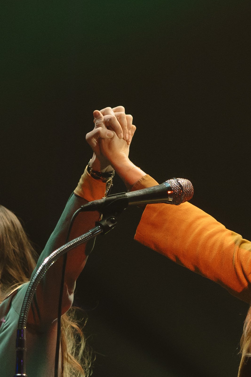 Two people holding hands in a fist bump above a microphone on stage. Aly and Aj concert event photographed by Rhianon Brown Photography.