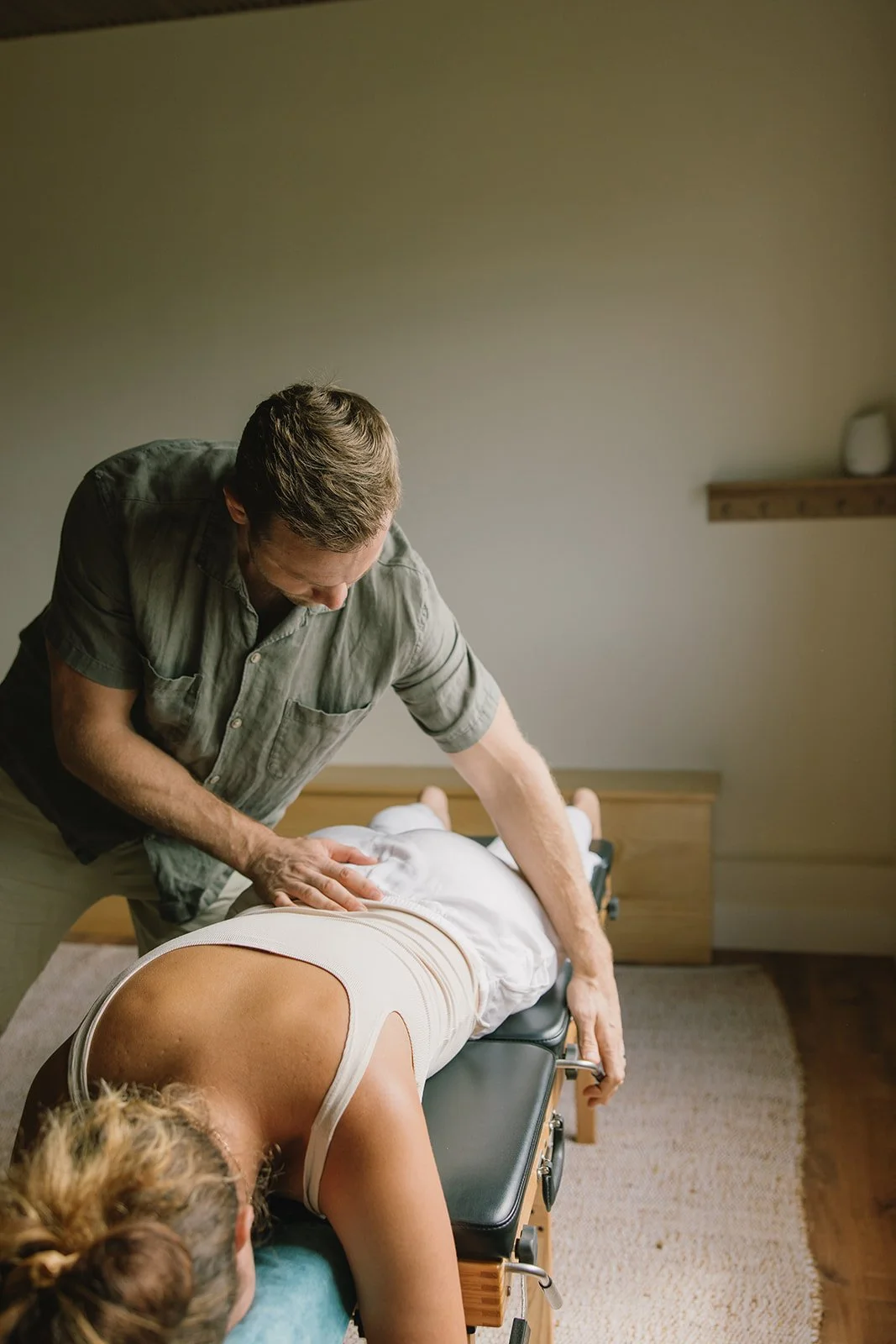 A chiropractor performing a back adjustment on a patient lying face down on an adjustment table in a treatment room. Brand and lifestyle photography session for Abundant Life Chiropractics in Maui, Hawaii by Rhianon Brown Photography.