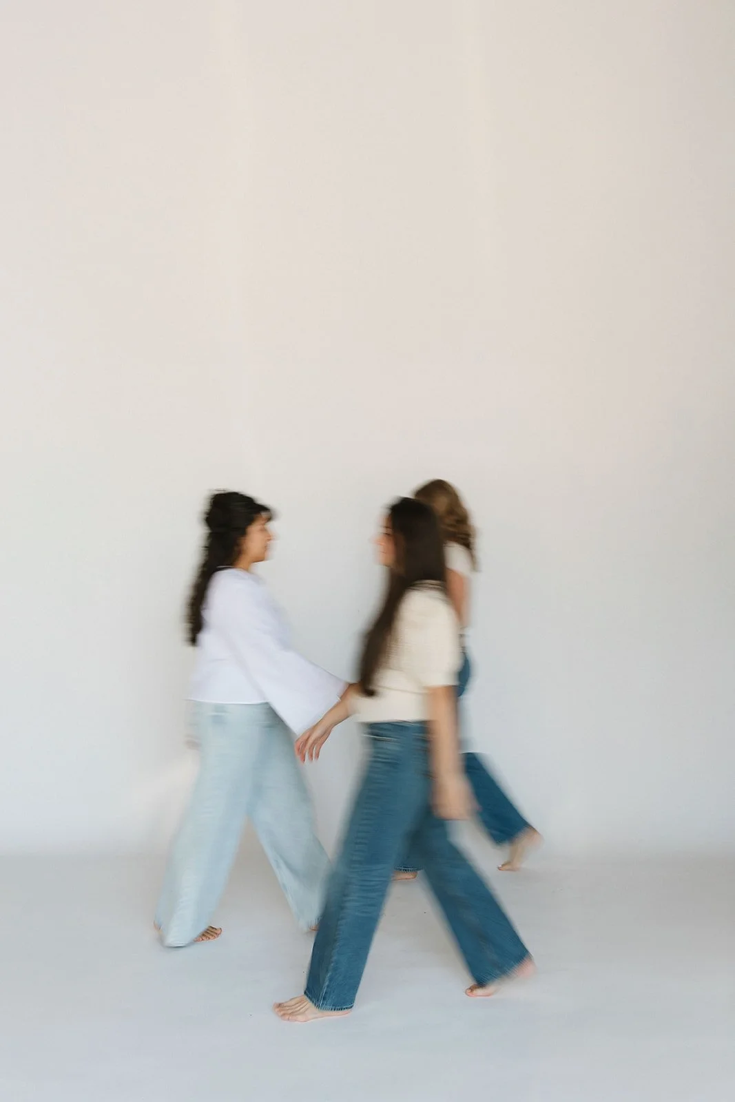 Three women walking and holding hands against a plain white background, wearing casual clothing. Branding photoshoot for Motherland Wellness by Rhianon Brown Photography in Springfield, Missouri.