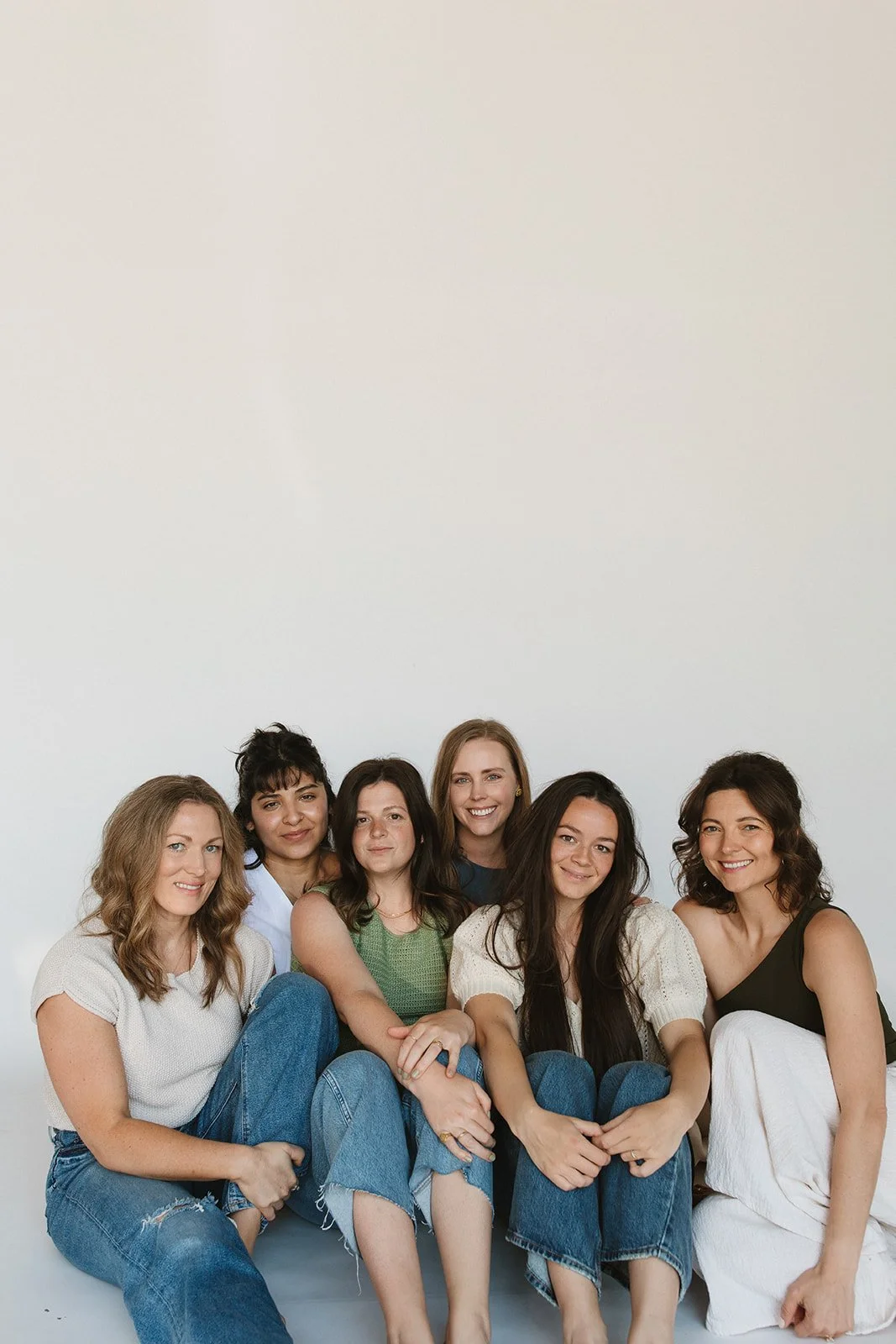 Eight women sitting close together, smiling against a plain white background. Branding photoshoot for Motherland Wellness by Rhianon Brown Photography in Springfield, Missouri.