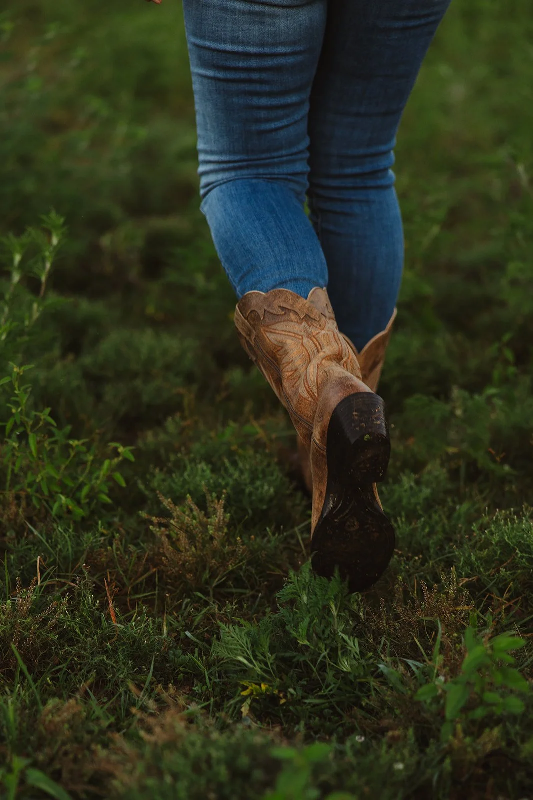 Person walking through grassy field, wearing blue jeans and cowboy boots.  Brand and lifestyle photography for Sacred Align Equine by Rhianon Brown Photography.