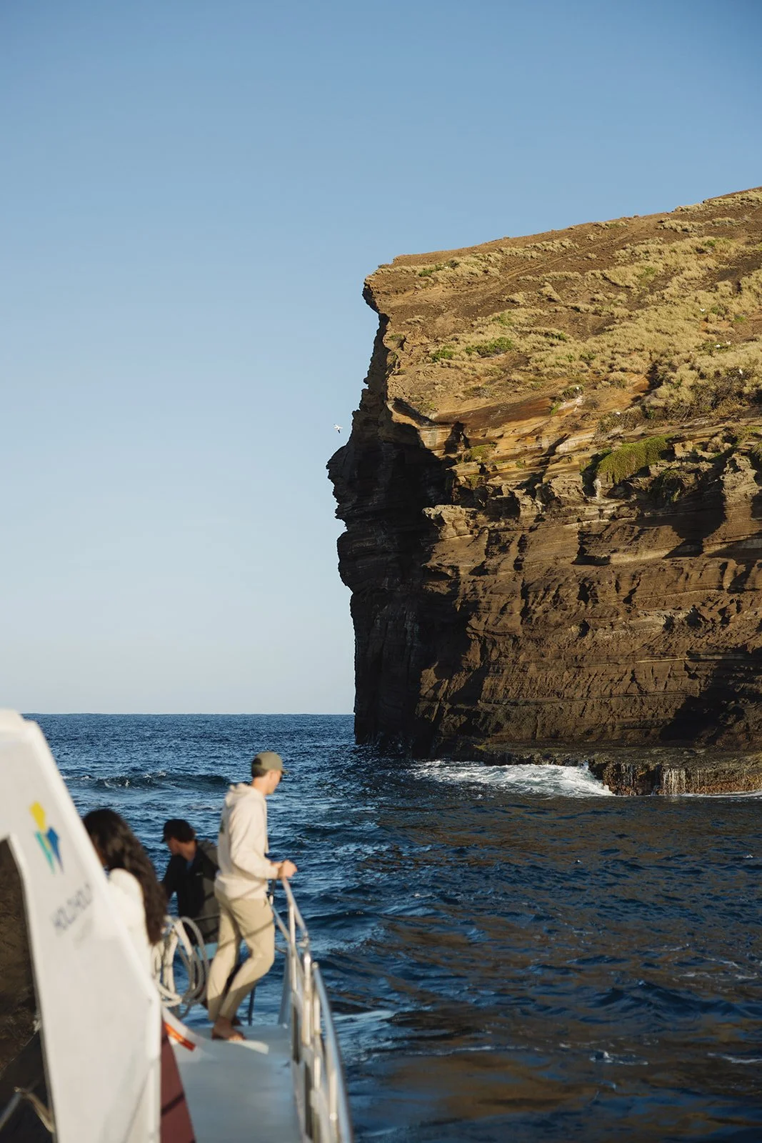 People on a boat near a large rocky coastal cliff during daytime. Brand and travel photography session for Holo Holo Charters in Kauai, Hawaii by Rhianon Brown Photography.