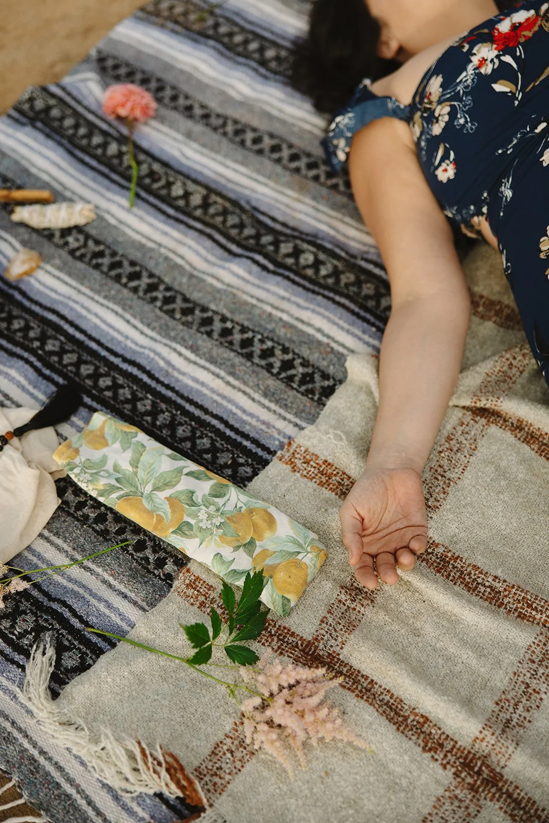 Person lying on a patterned outdoor rug with flowers and a wrapped gift nearby. Brand and lifestyle photography for Connie Neyra and yoga practitioner by Rhianon Brown Photography.