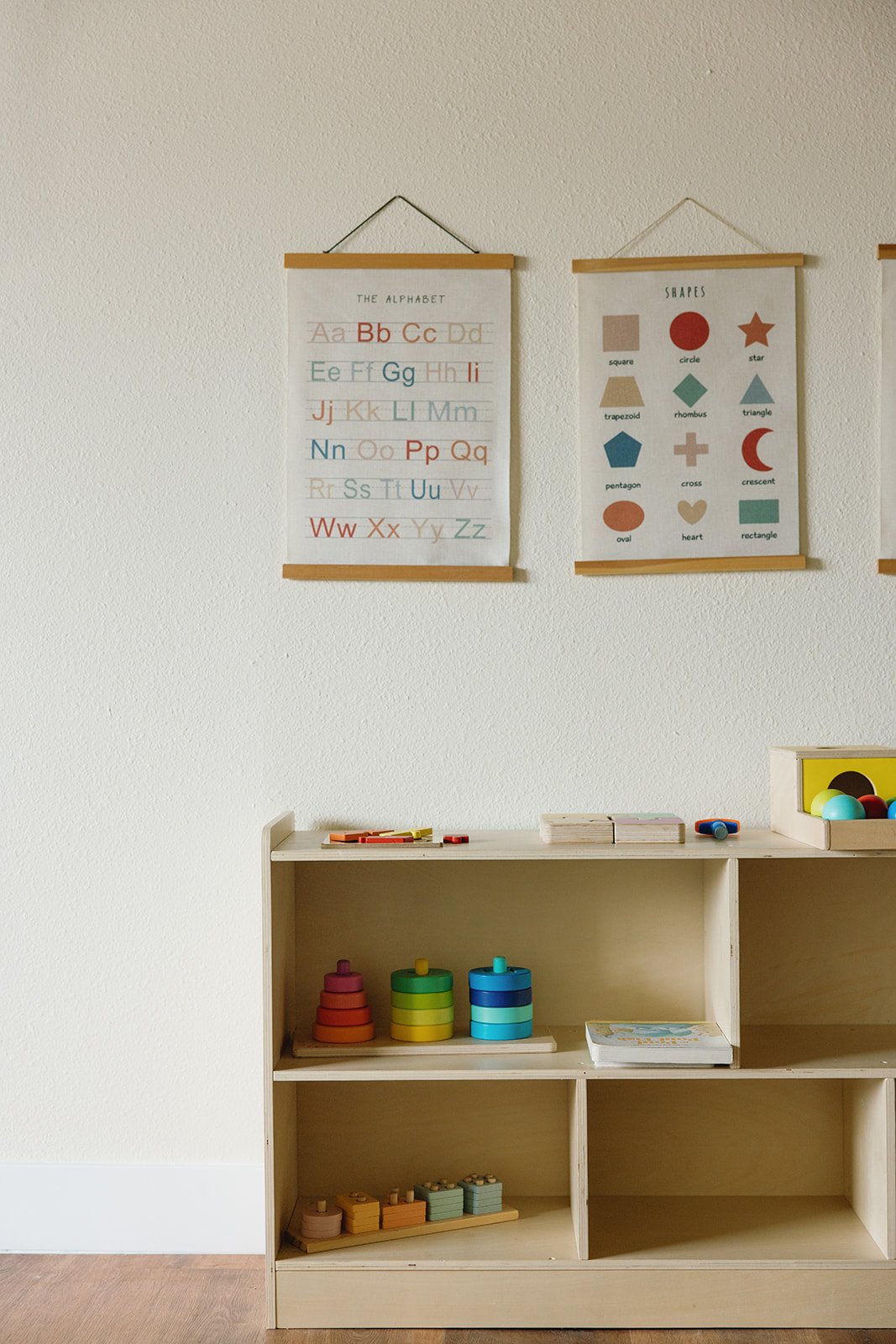 Educational display in a classroom, showing alphabet and shape posters, with wooden shelves holding educational toys and books. Brand and lifestyle photography session for Abundant Life Chiropractics in Maui, Hawaii by Rhianon Brown Photography.
