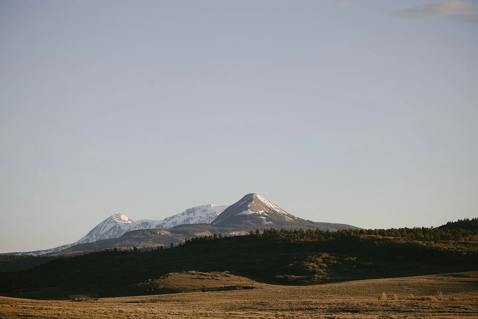 Mountain landscape with snow-covered peaks in the background and grassy plains in the foreground. Rhianon Brown Photography's brand photoshoot for Grace Reins Equine Therapy in Colorado.