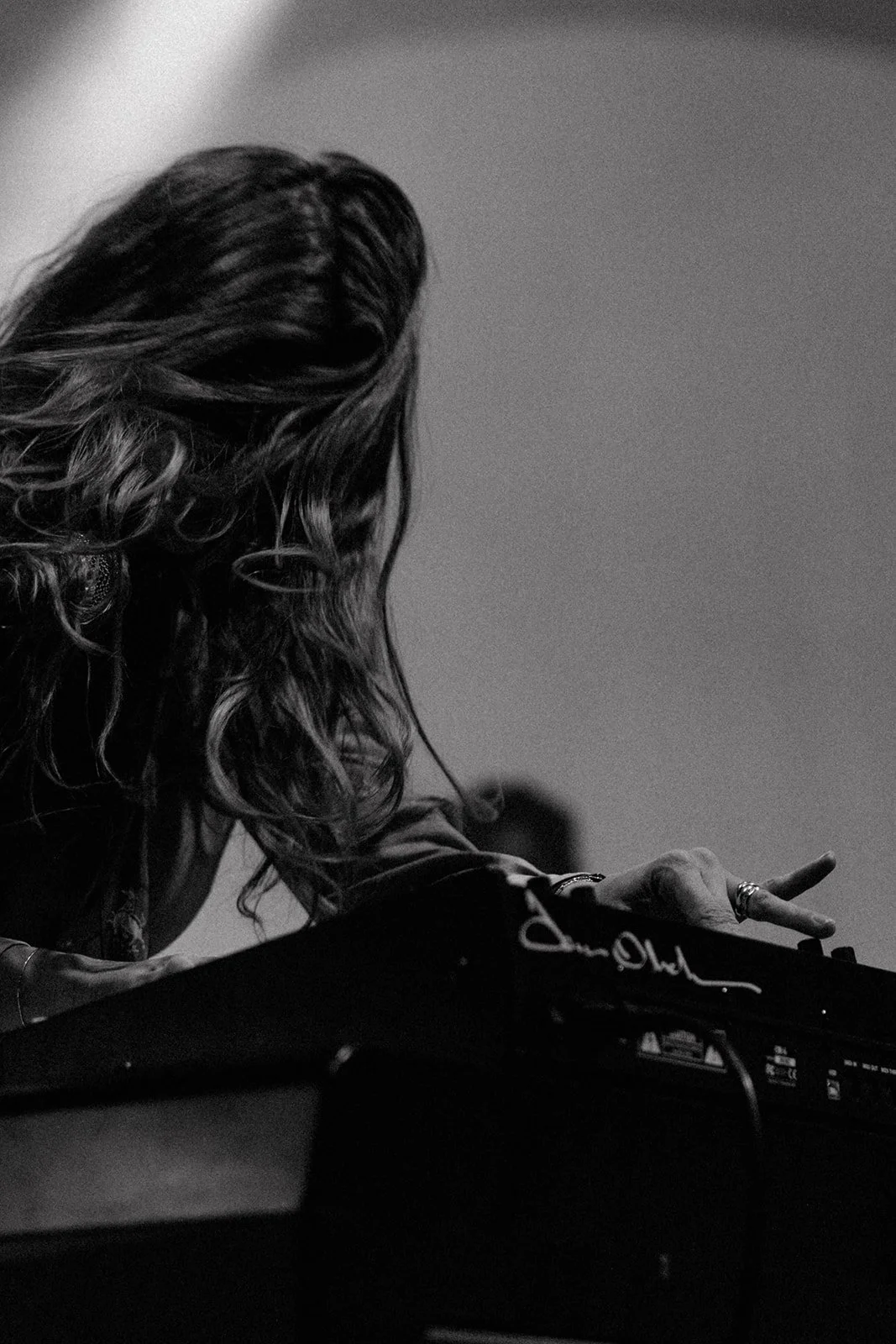 A woman with curly hair appears to be DJing or working with music equipment, with her hand pointing or adjusting a control button. Aly and Aj concert event photographed by Rhianon Brown Photography.