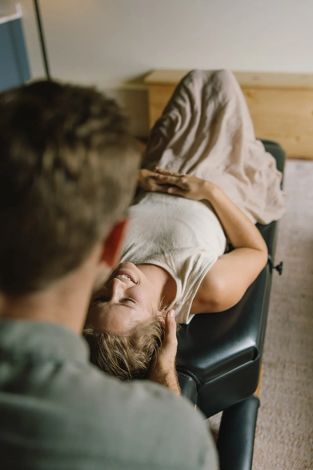 A woman lying on a bed, smiling and touching her hair, while a man gently holds her head and looks at her. Brand and lifestyle photography session for Abundant Life Chiropractics in Maui, Hawaii by Rhianon Brown Photography.