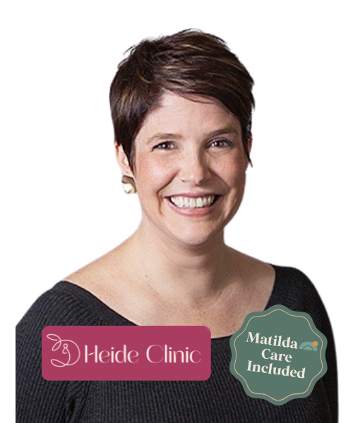 Smiling woman with short brown hair wearing a black top, with a Heide Clinic logo and a badge that says 'Matilda Care Included'.