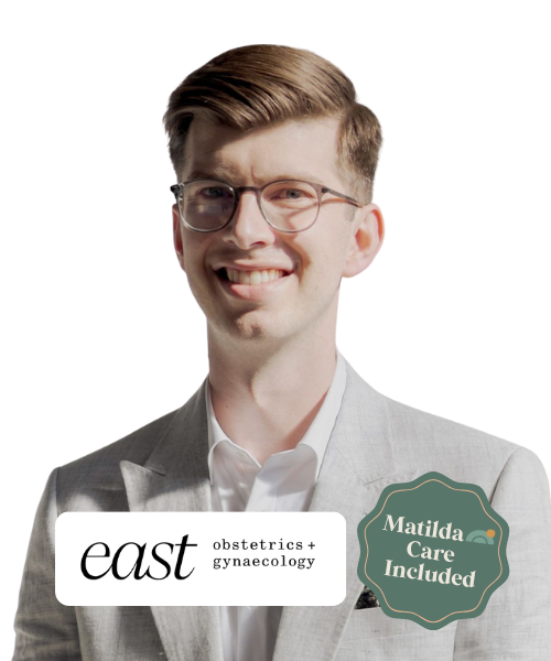 A young man with glasses and light brown hair, wearing a light gray suit and white shirt, smiling at the camera. The image includes text indicating 'east obstetrics + gynaecology' and a badge that says 'Matilda Care Included.'