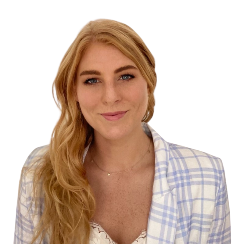A woman with long, wavy blonde hair and blue eyes is smiling at the camera. She is wearing a light-colored, checkered shirt over a white lace top and a delicate necklace.