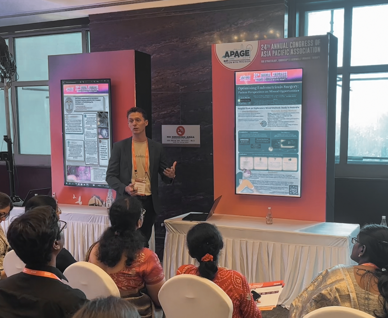 A male presenter giving a talk to a seated audience at APAGE.