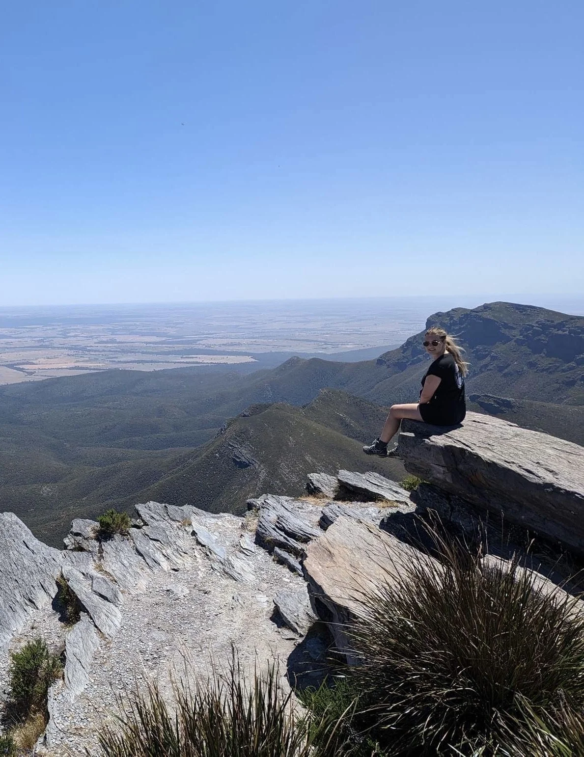 Anna, a woman with a lived experience of endometriosis, sitting on a rock overlooking a valley.