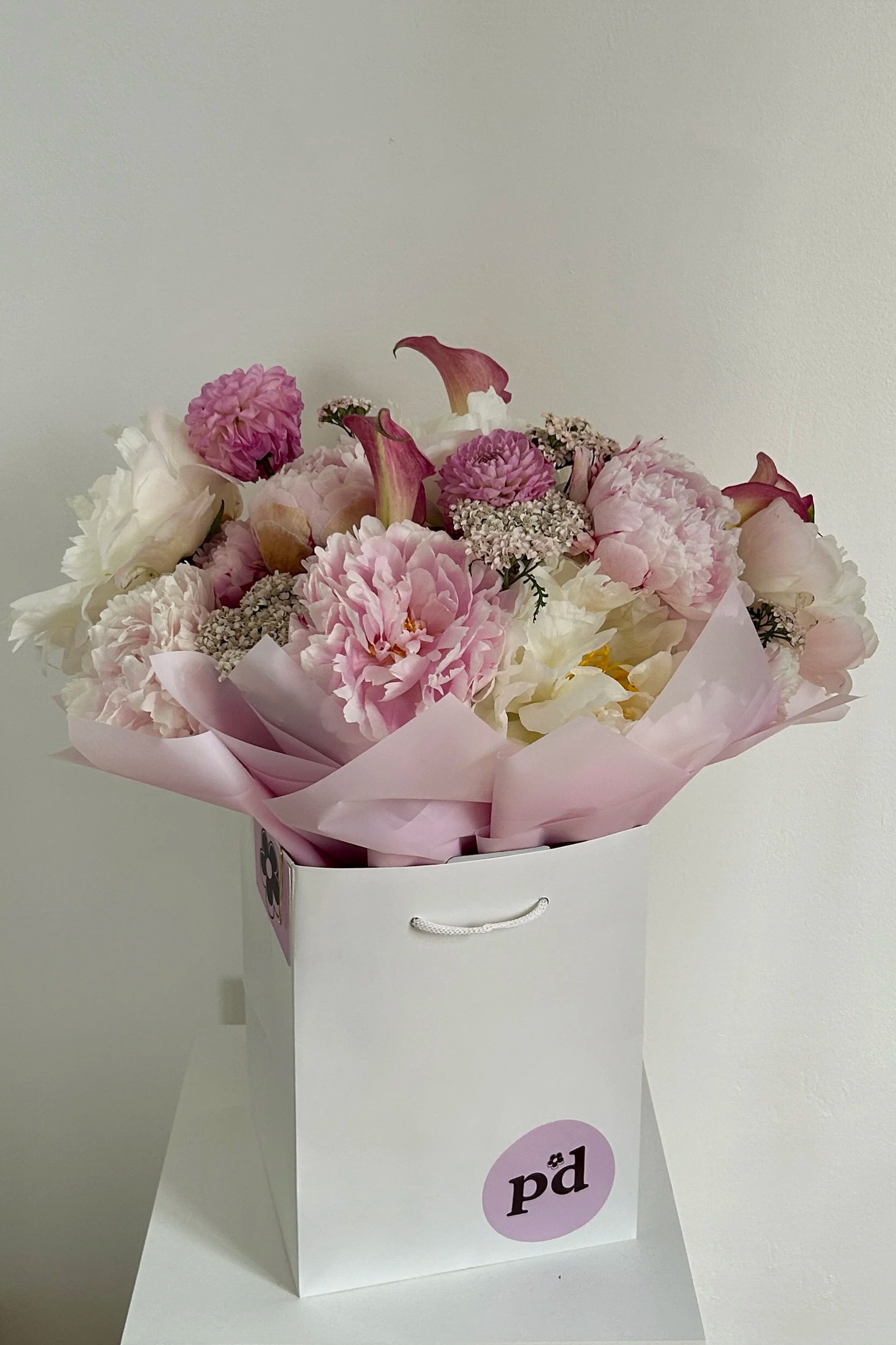 A  luxury pink and white bouquet, in a white gift bag, with peonies, dahlias, cala lilies, made by Petal'd