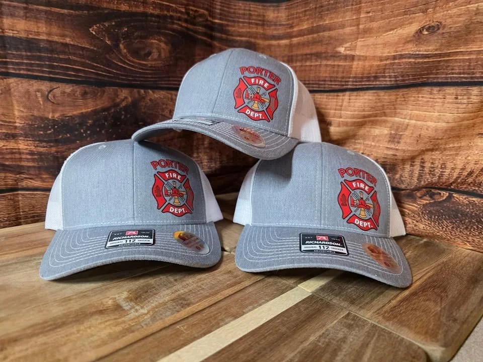 Three baseball caps with the Porter Fire Department emblem on the front, placed on a wooden surface with a wood-paneled background.