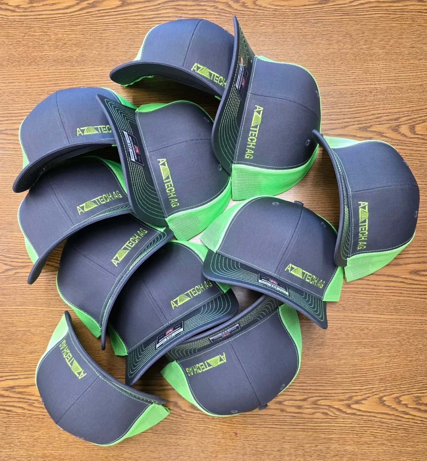 Multiple black and green baseball caps with 'AZTECH' logo on wooden surface.