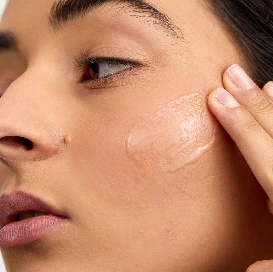 Close-up of a woman's face applying moisturizer or skincare product on her cheek with her finger.