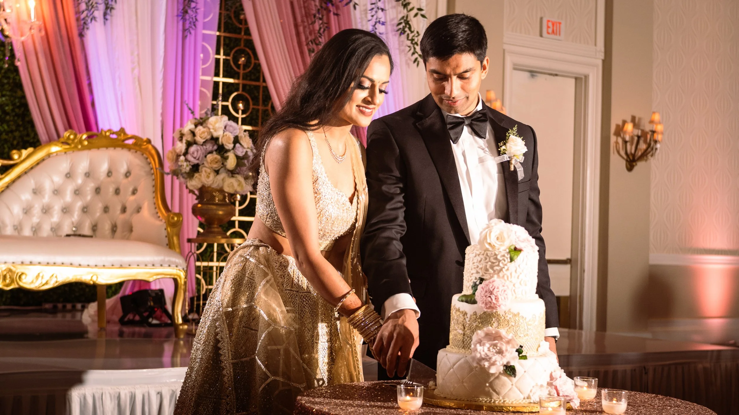 A bride and groom cutting a wedding cake together at their wedding reception, decorated with flowers and elegant furnishings.