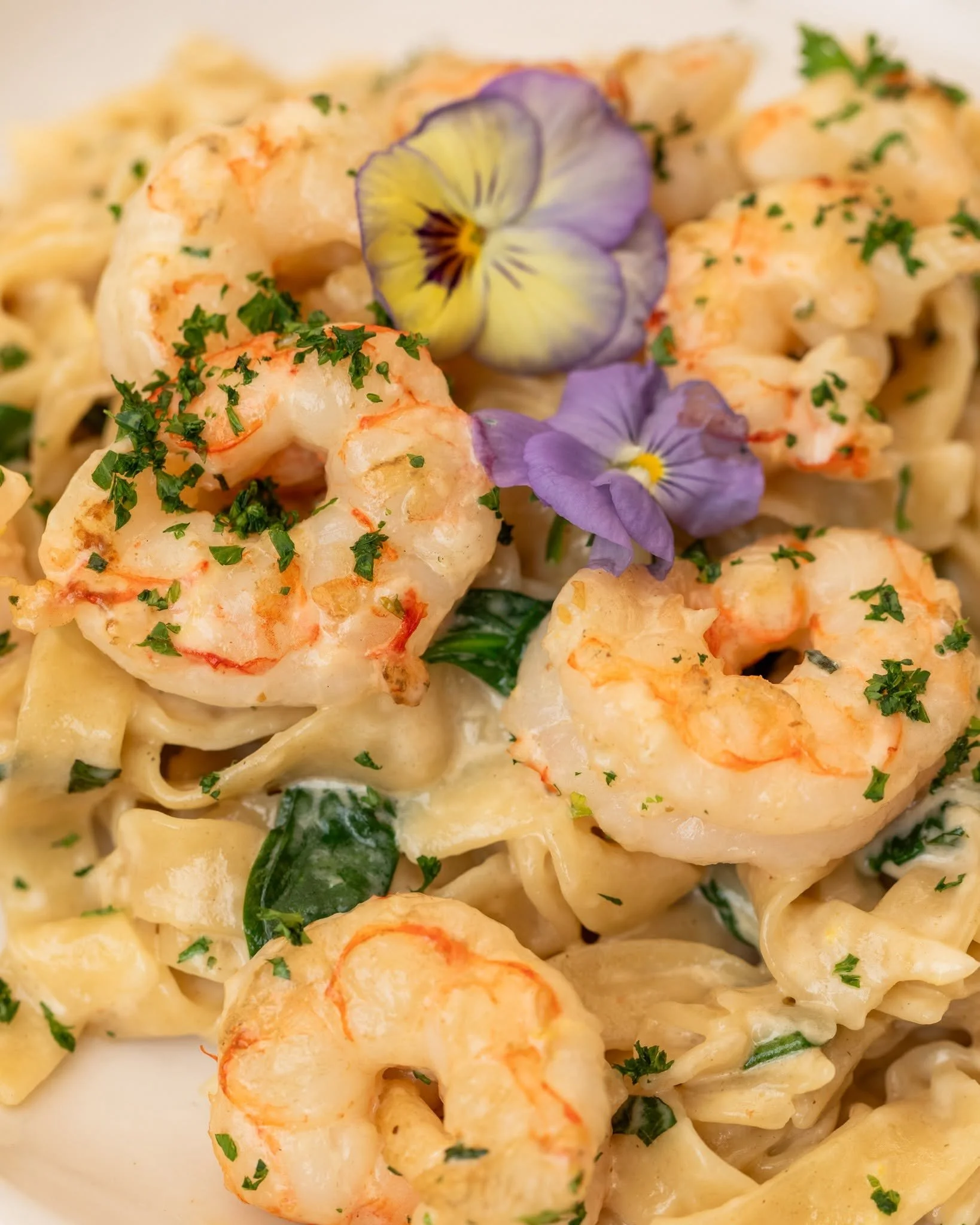 Close-up of cooked shrimp pasta dish topped with chopped parsley and edible flower petals.