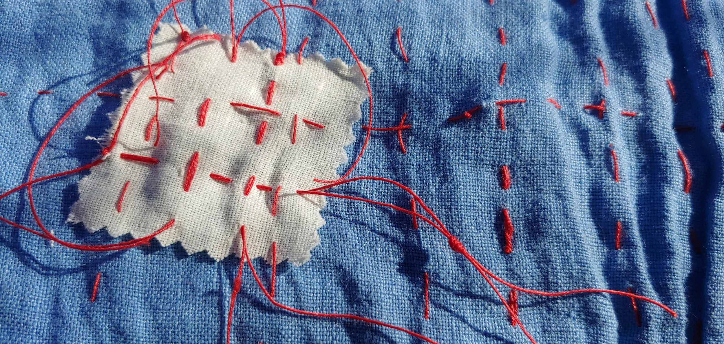 A close-up of a piece of blue fabric with white fabric stitched onto it, surrounded by red embroidery thread.