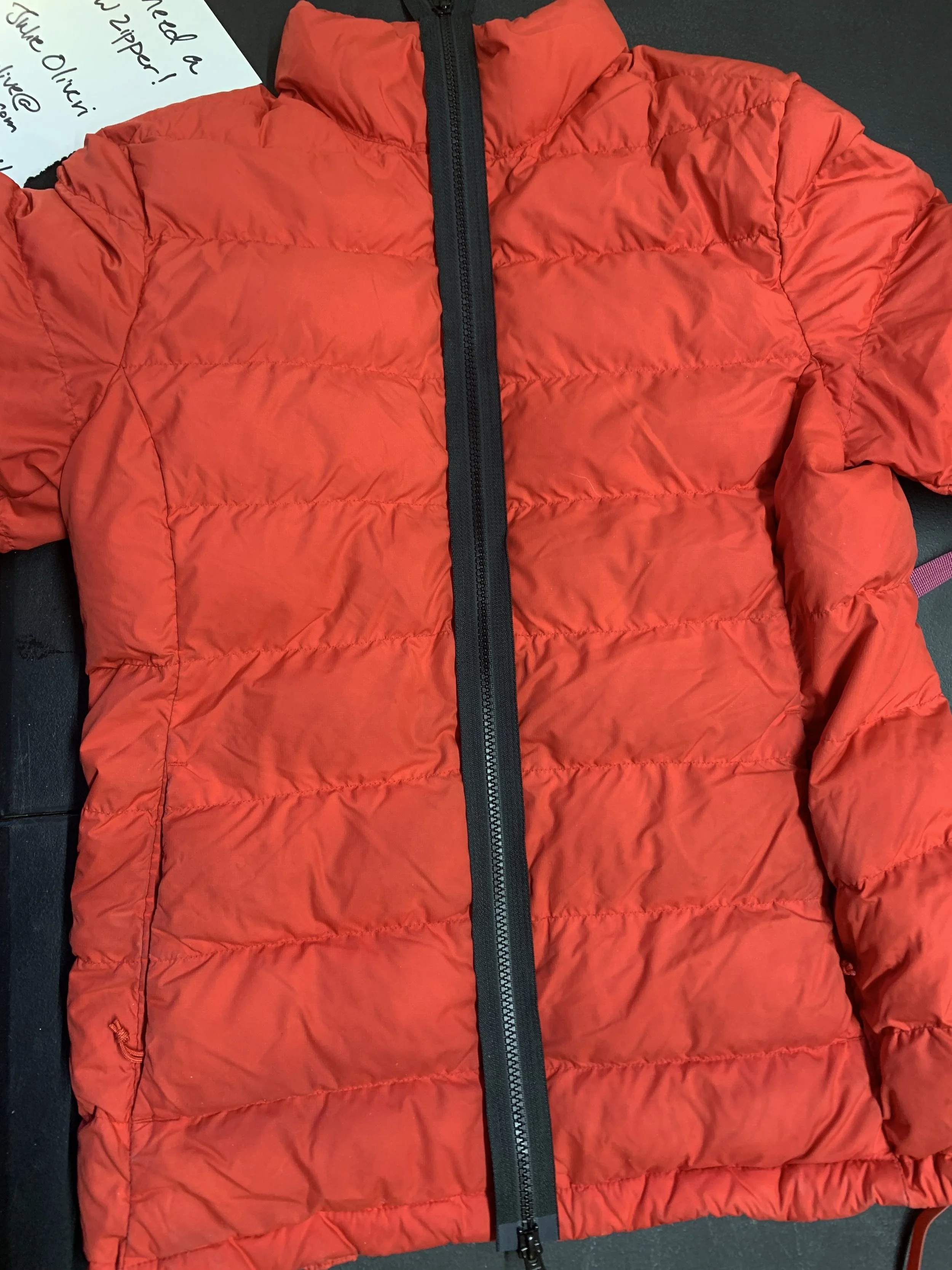A bright red puffy winter jacket with a black zipper down the center laying on a black surface.
