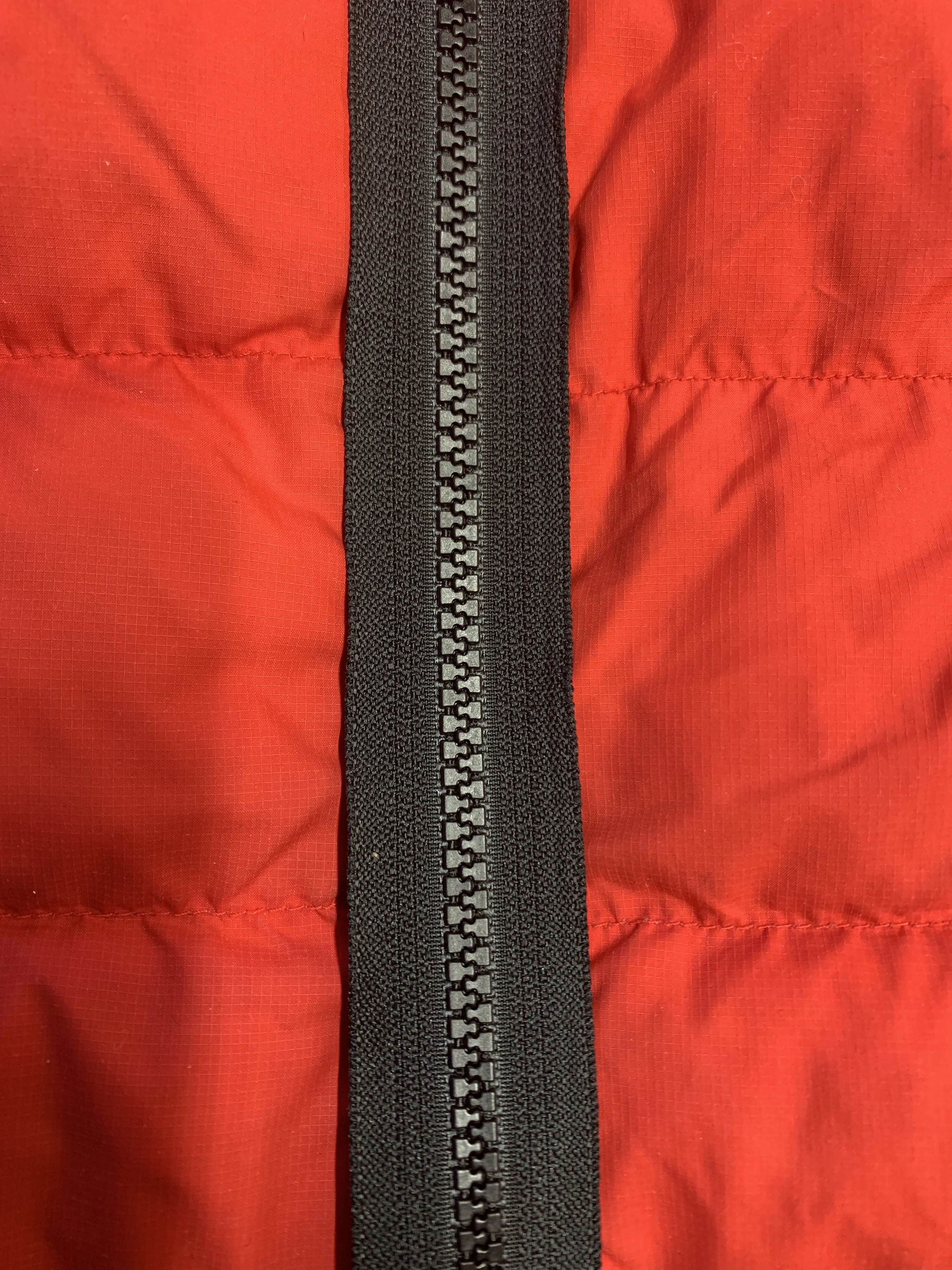 Close-up of a red nylon jacket with a black zipper and black trim.