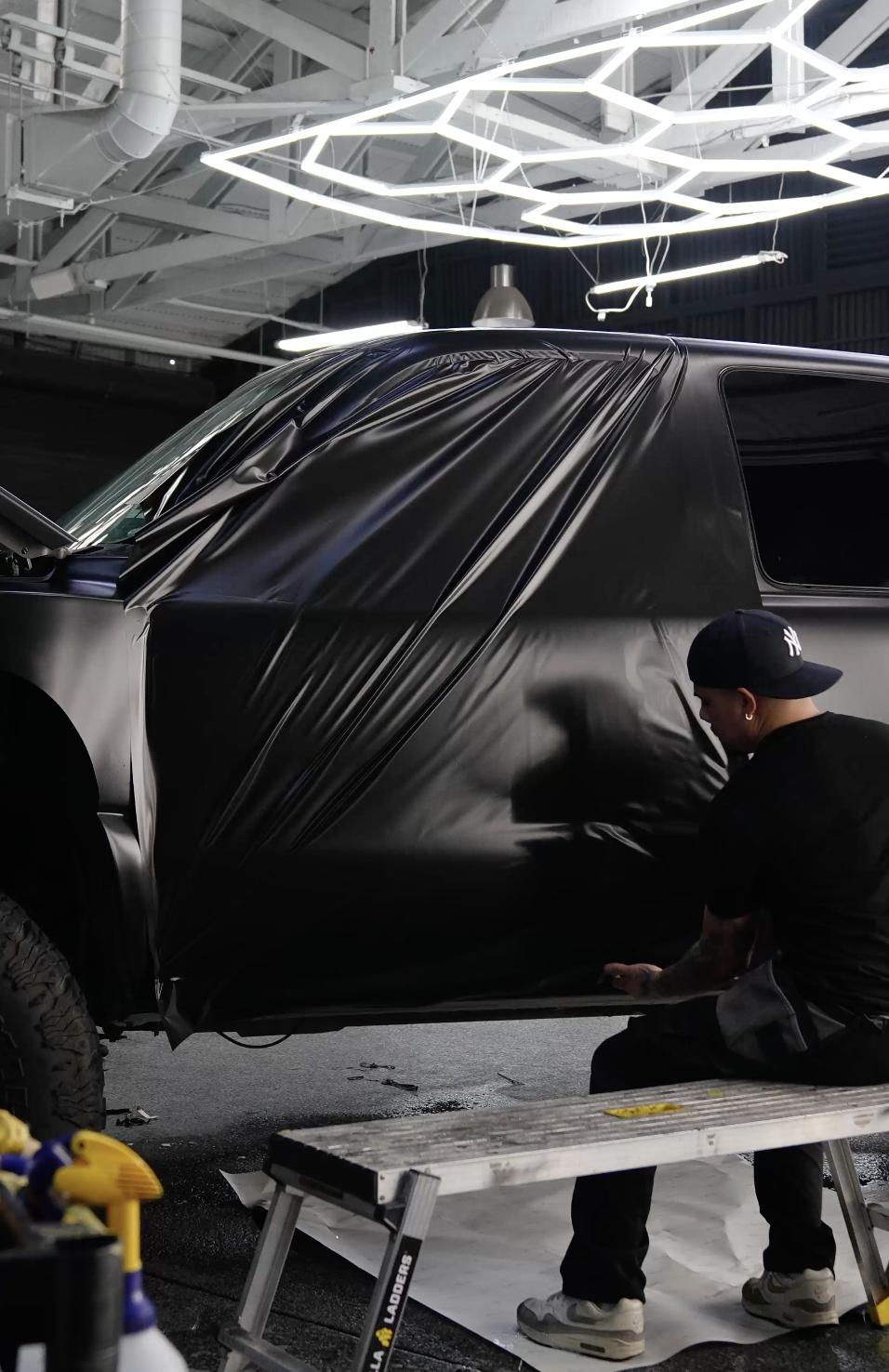 A black vinyl wrap being installed on a Chevy truck to transform it's look done by Reborn Motorwerks.