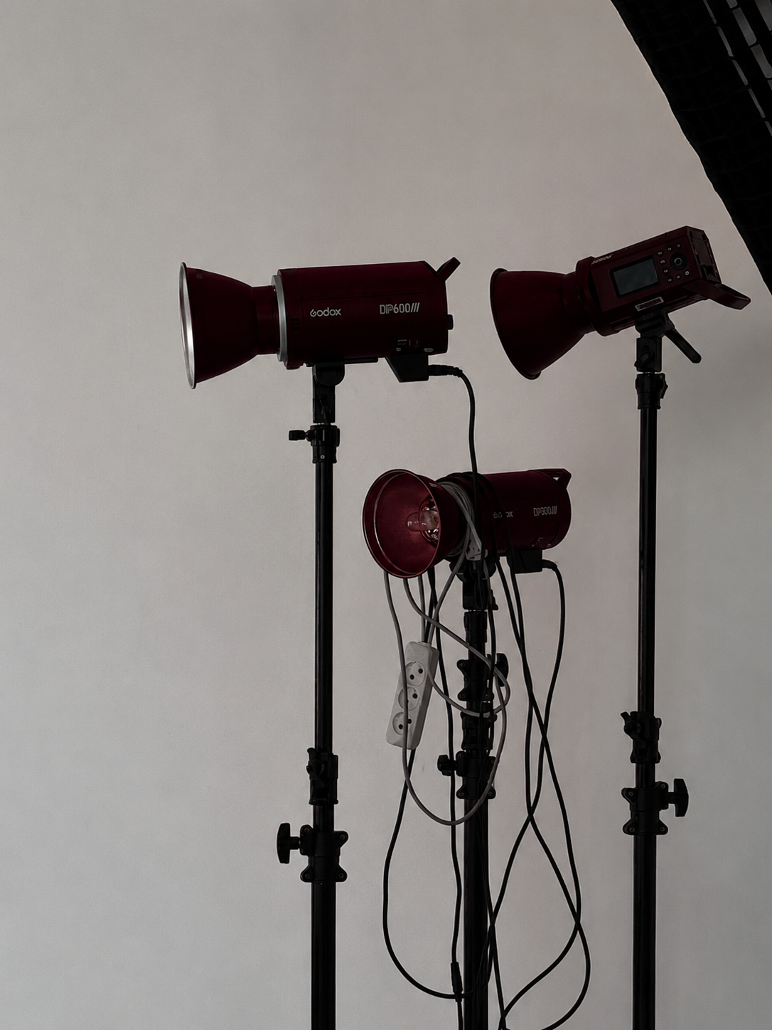 Studio lighting equipment including three red studio lights on stand, with cables and power strip, against a plain gray background.