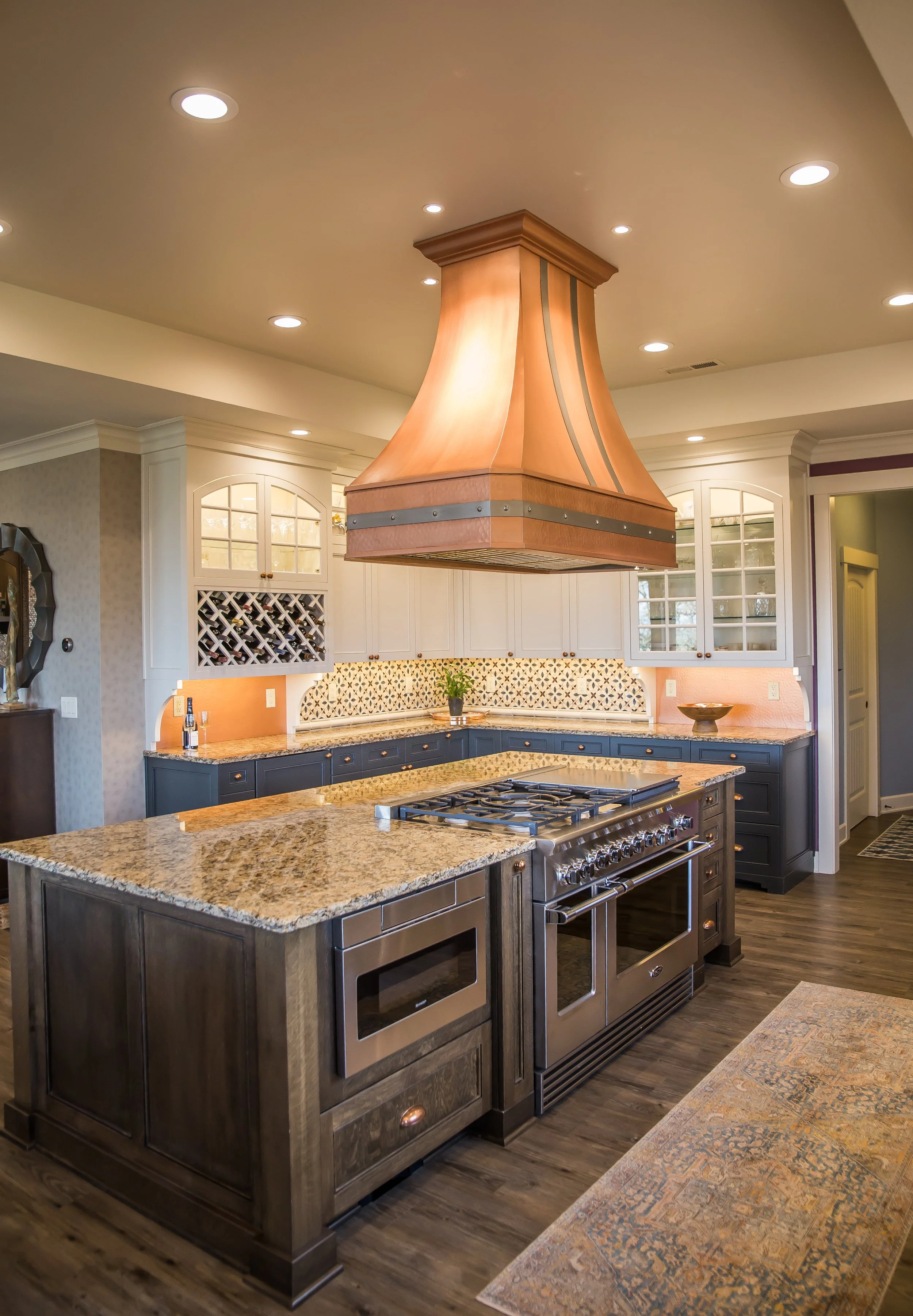 A modern kitchen with a large wooden island and a stove, white cabinets, a decorative backsplash, and a copper range hood.