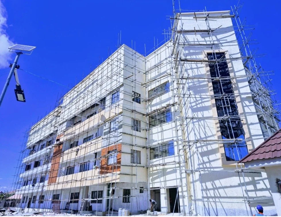 Construction site with scaffolding around a multi-story white building against a clear blue sky.