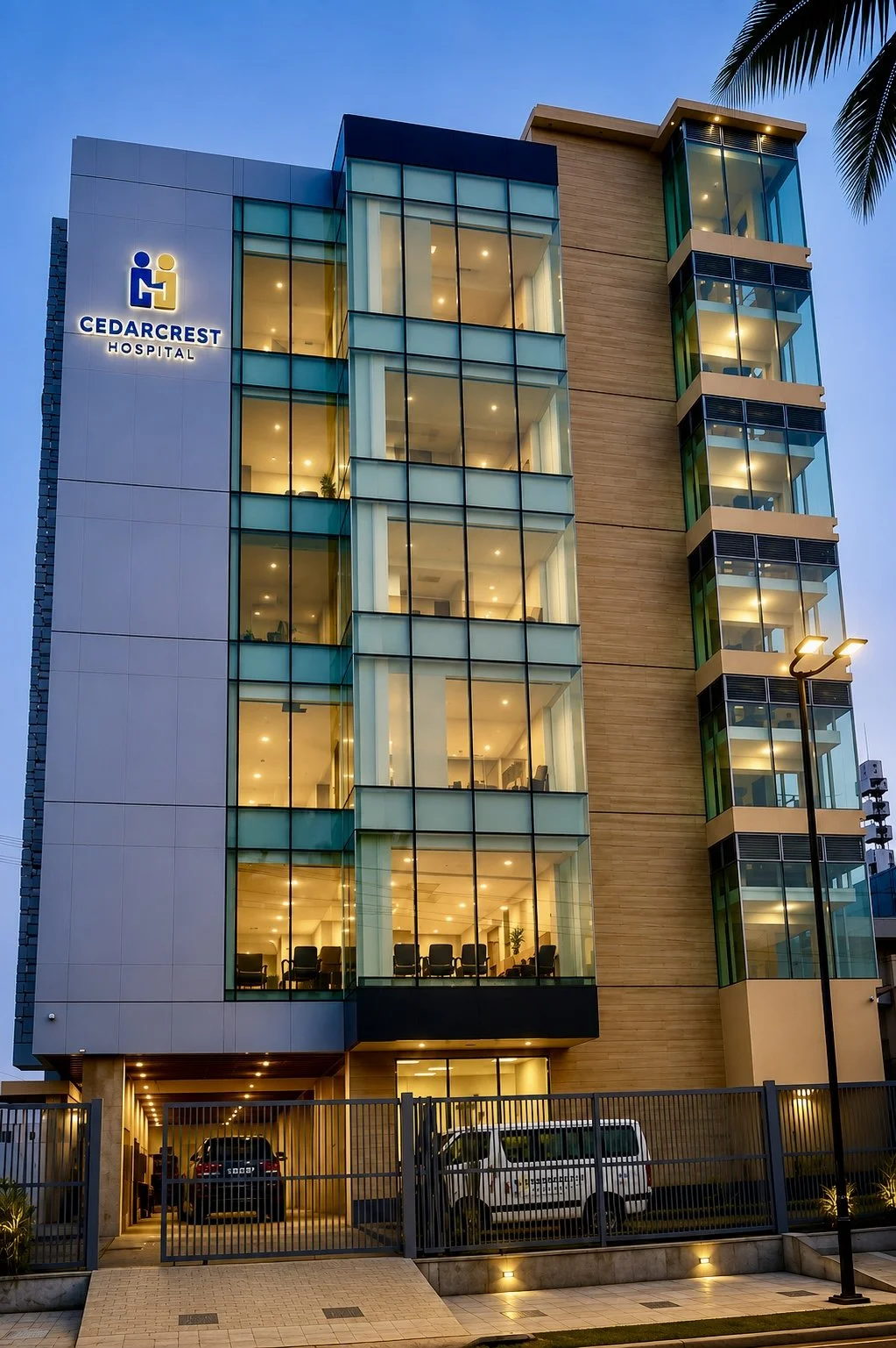 Modern hospital building with glass windows and illuminated interior, marked with Cedarcrest Hospital sign and logo, with parking area and street lamp outside during evening.