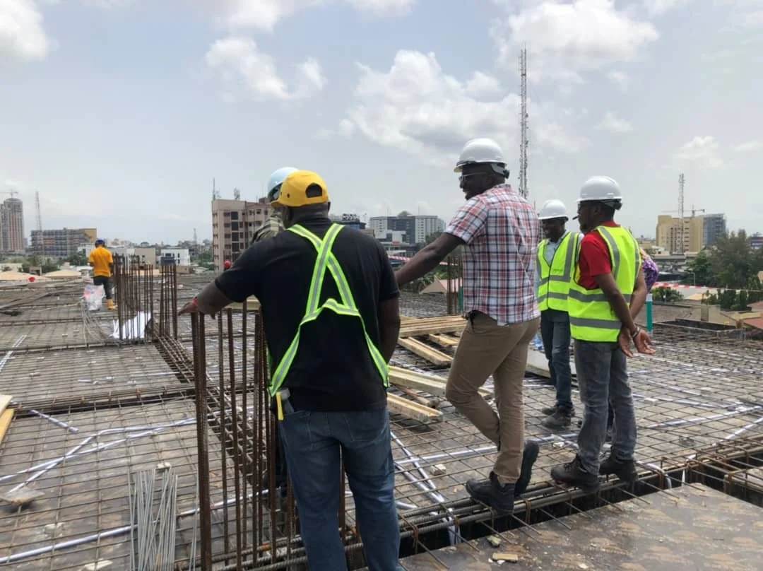 Group of construction workers wearing safety helmets and vests inspecting a building under construction in an urban area.