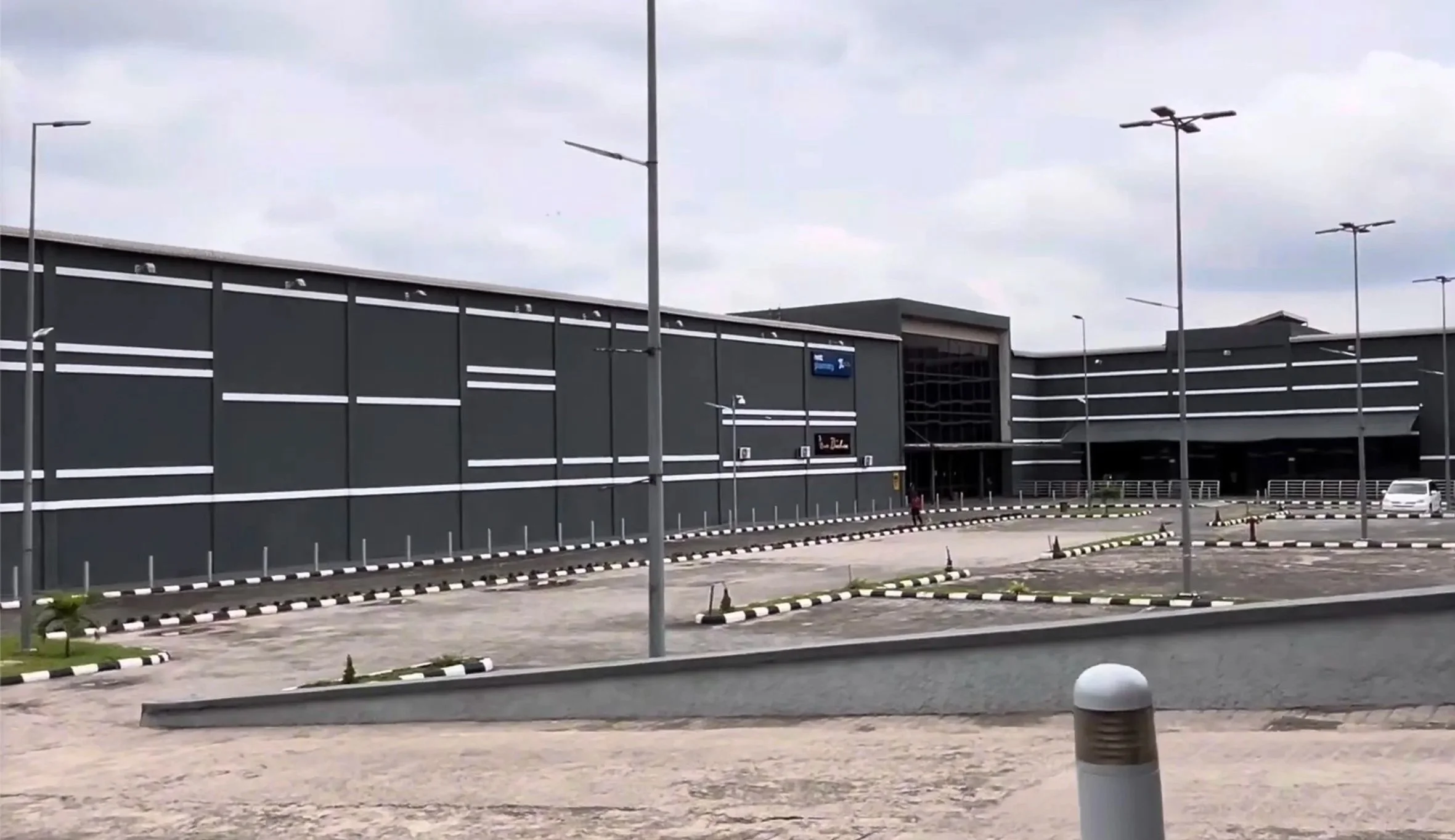 Large commercial building with a modern design, dark exterior, and white horizontal lines, situated in a mostly empty parking lot.