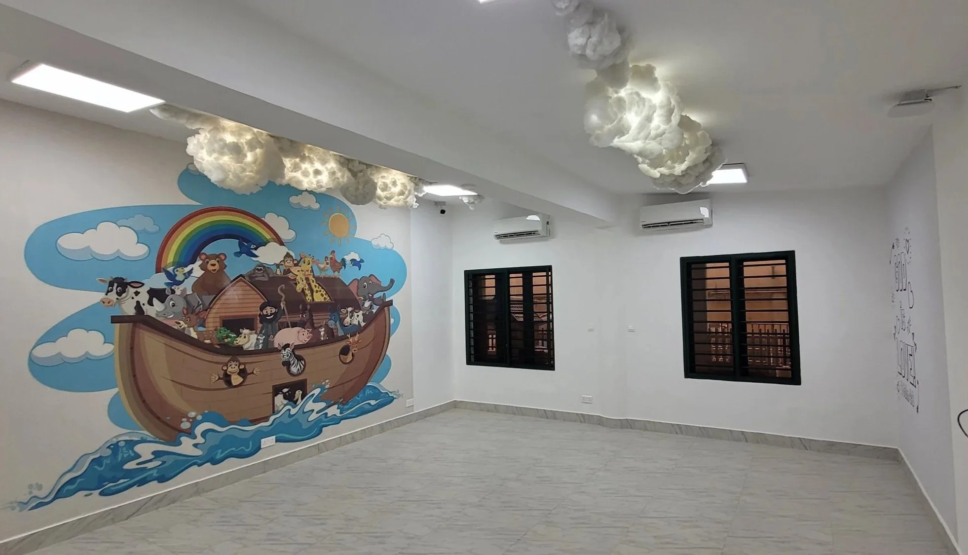 Interior room with cloudy cloud-shaped ceiling lights, a colorful mural of Noah's Ark with various animals, two dark-framed windows, and white walls.