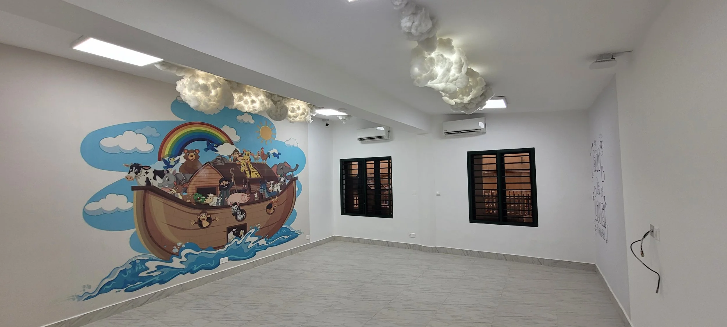Empty room with a colorful jungle animal mural on the wall, clouds hanging from the ceiling, and two windows with black frames within the children’s church building (RCCG Olive Branch) Project Managed by IHOD.